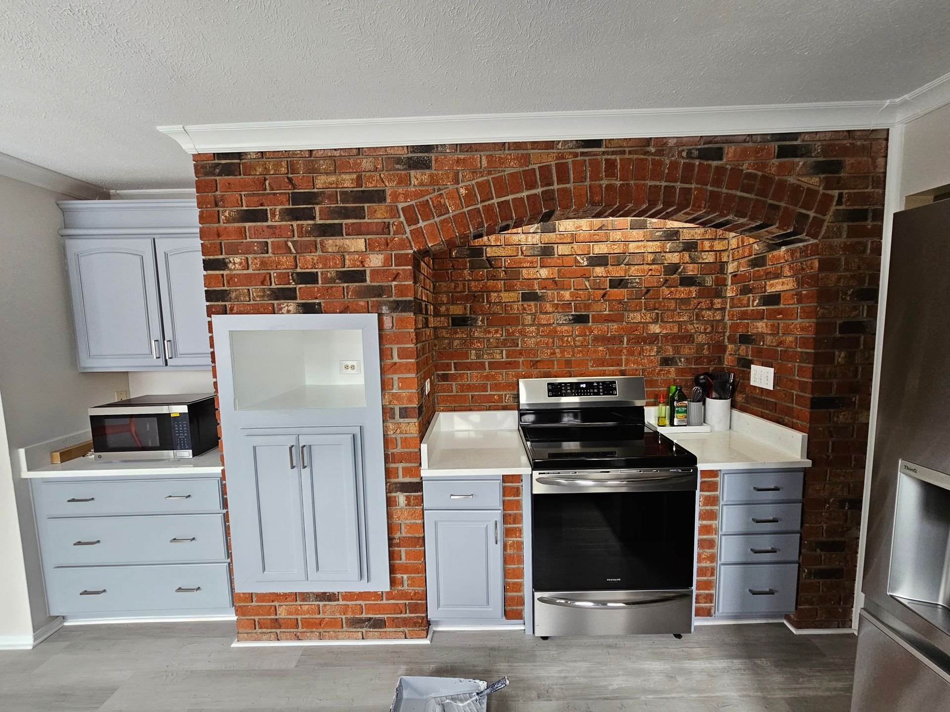 Kitchen with exposed brick accent wall, white cabinets, and a stainless steel stove under a brick arch.