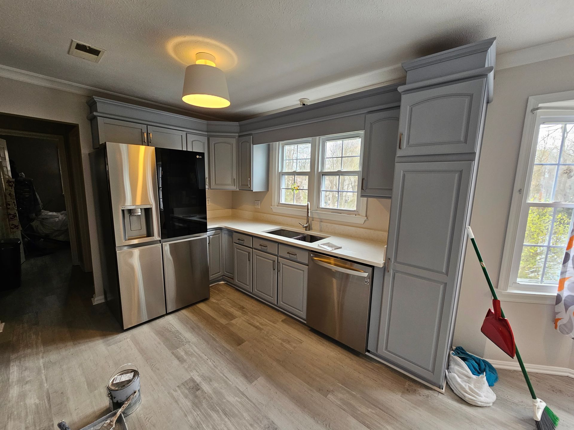 Bright kitchen with stainless steel fridge, white cabinets, wood floor, and a mop by the window.