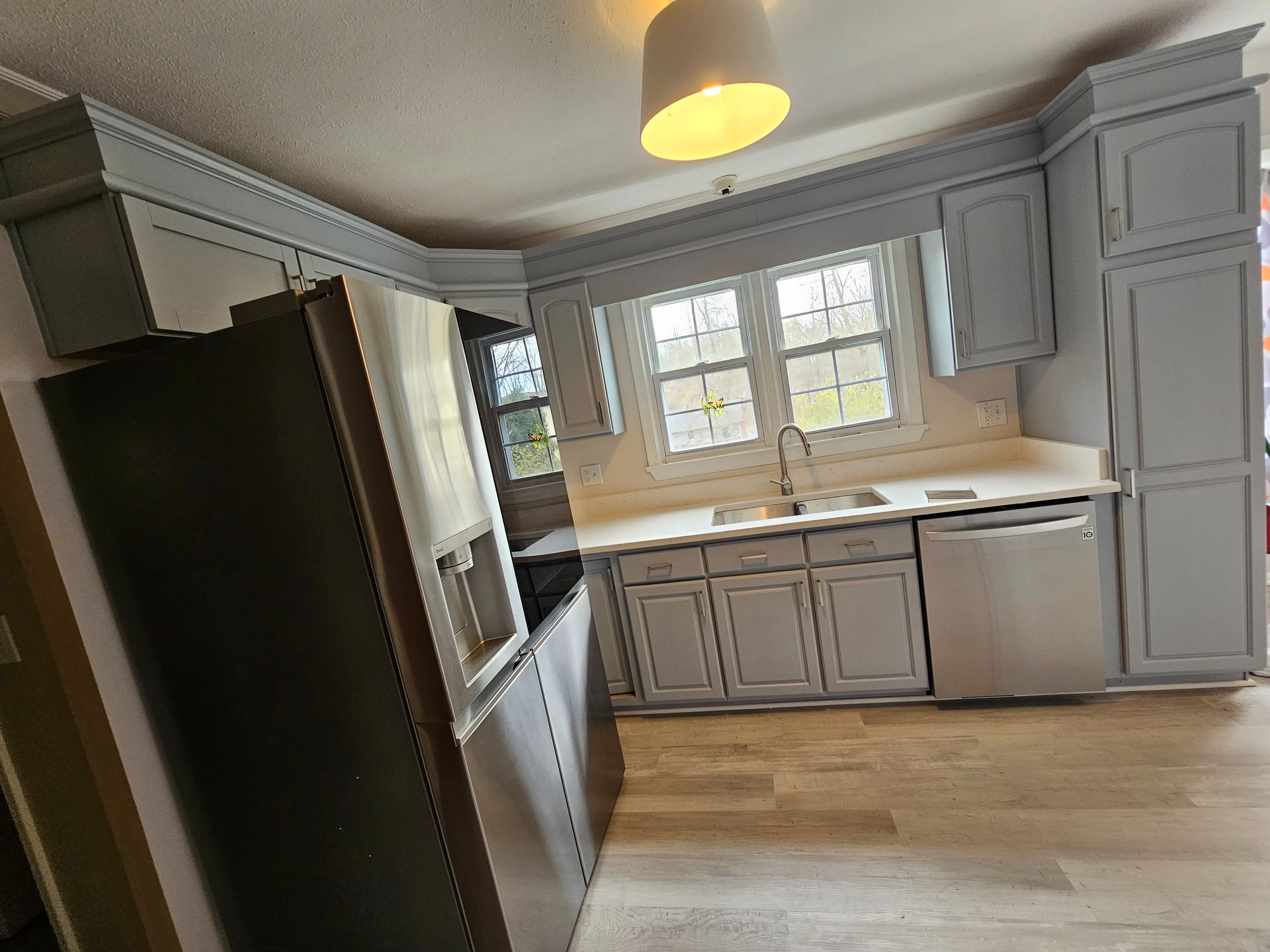 Small gray kitchen with cabinets, sink, dishwasher, and a window over a light wood floor.