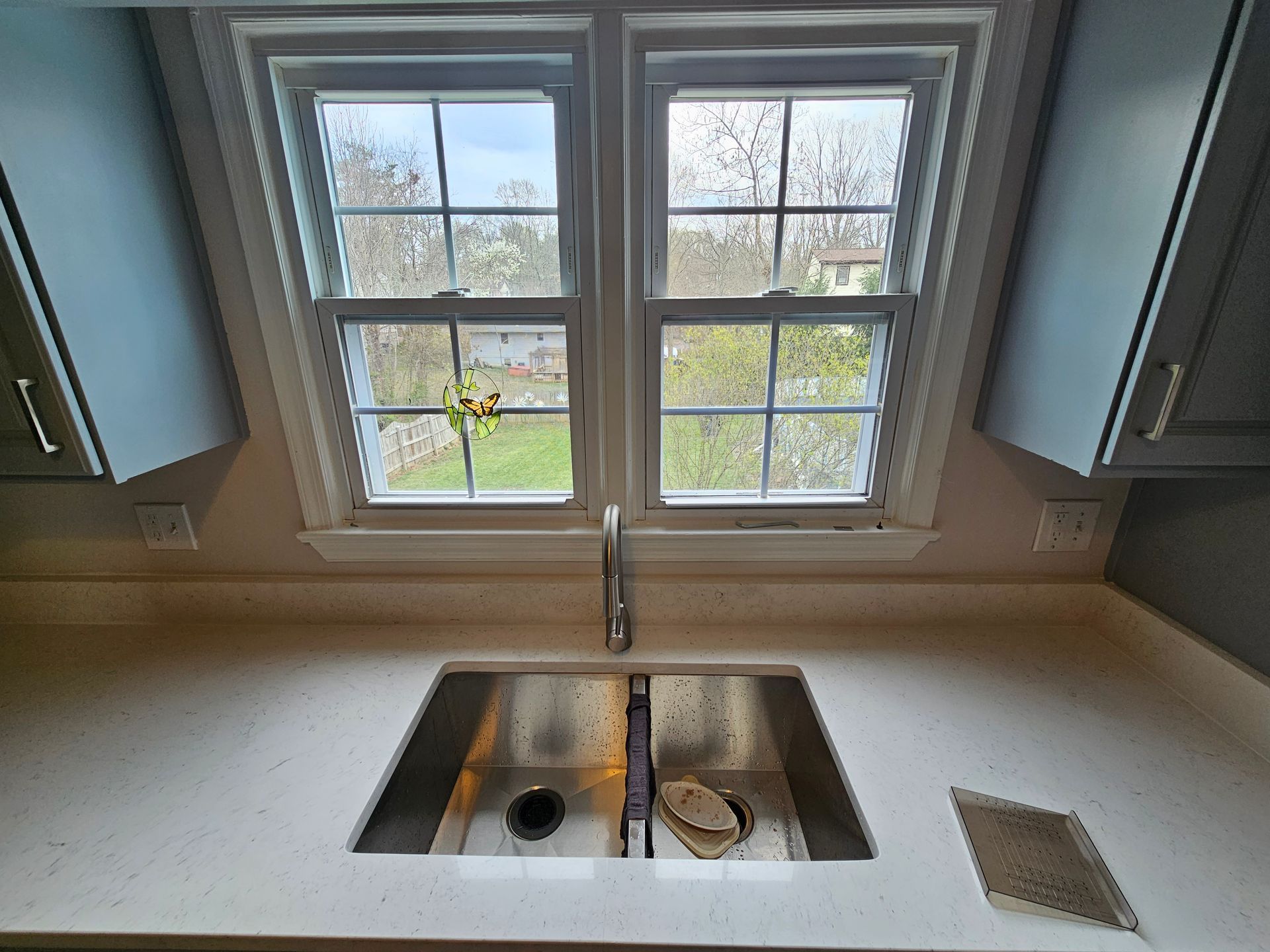 Kitchen sink beneath two windows with a stainless-steel basin and beige countertop