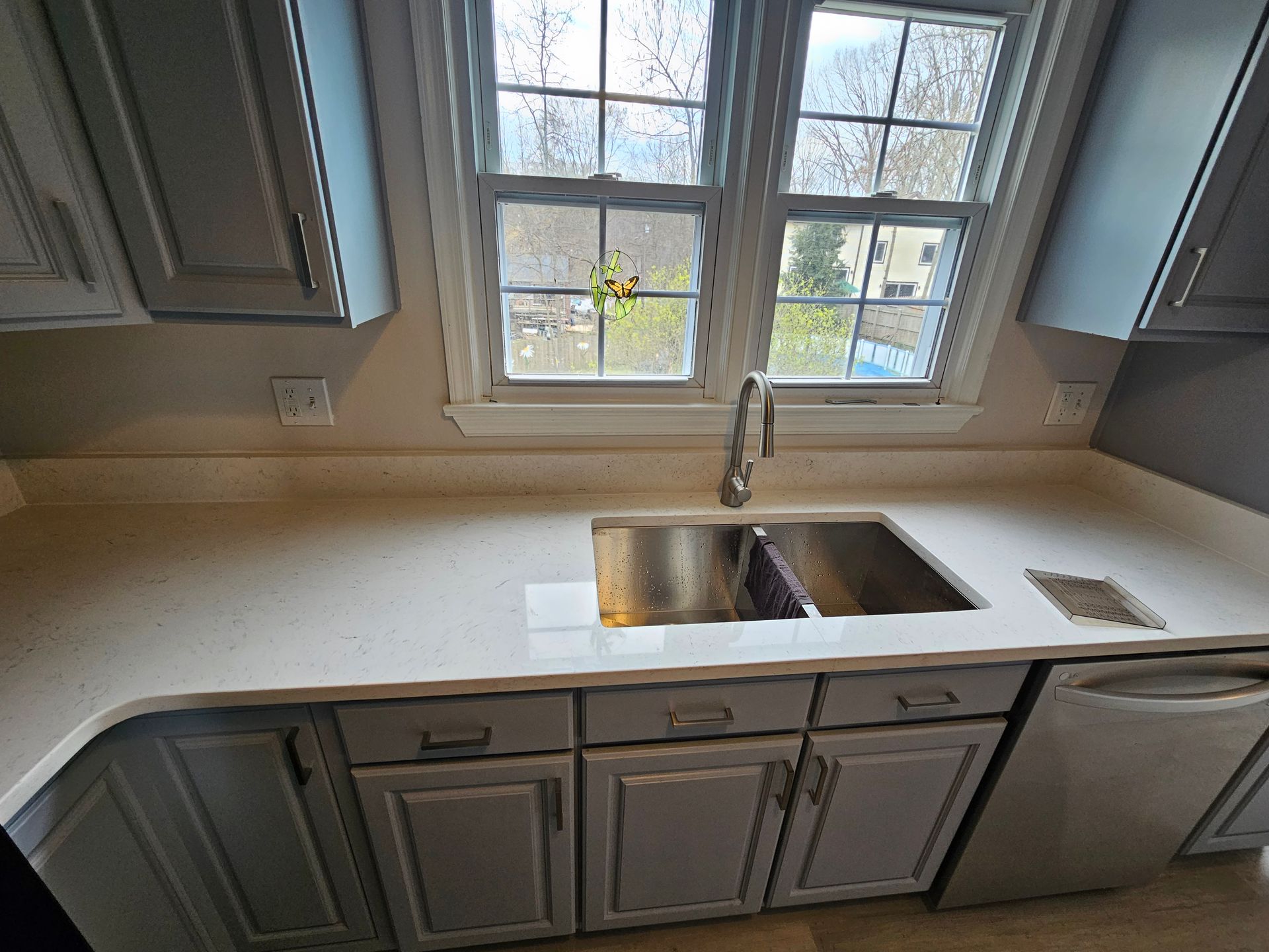 Kitchen sink beneath a window, with gray cabinets and light countertops.