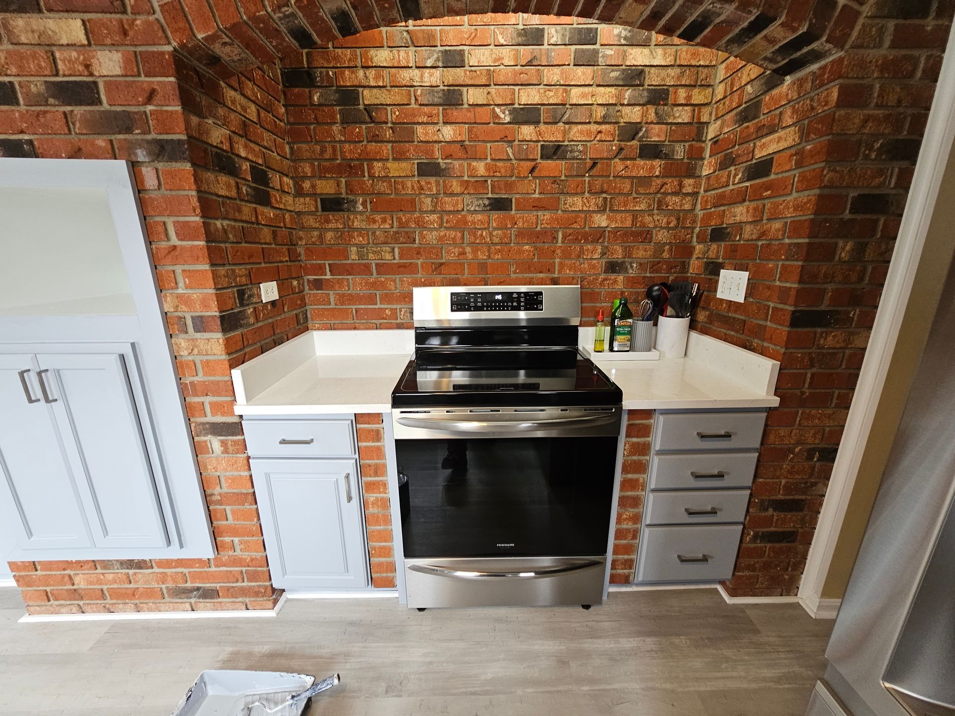 Kitchen alcove with brick arch, white cabinets, and stainless steel stove and oven