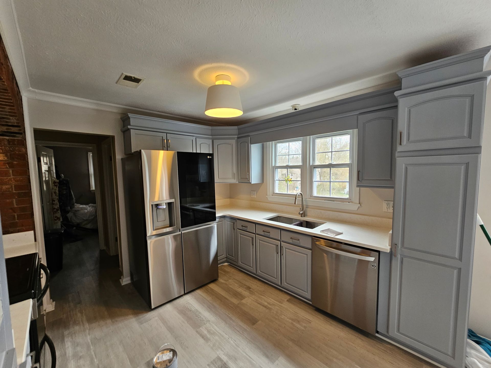 Modern kitchen with gray cabinets, stainless steel fridge, white countertops, and wood-look flooring