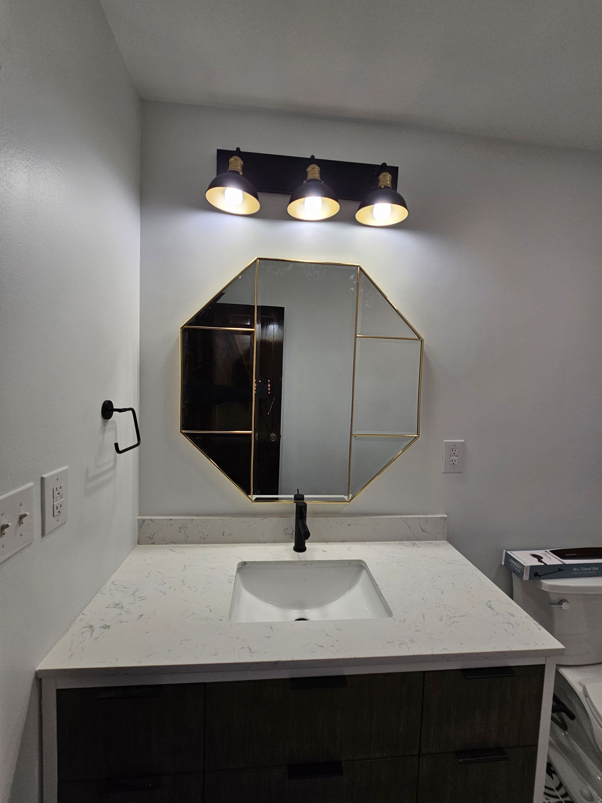 Bathroom vanity with octagonal mirror, three-light fixture, white countertop, and dark cabinet.