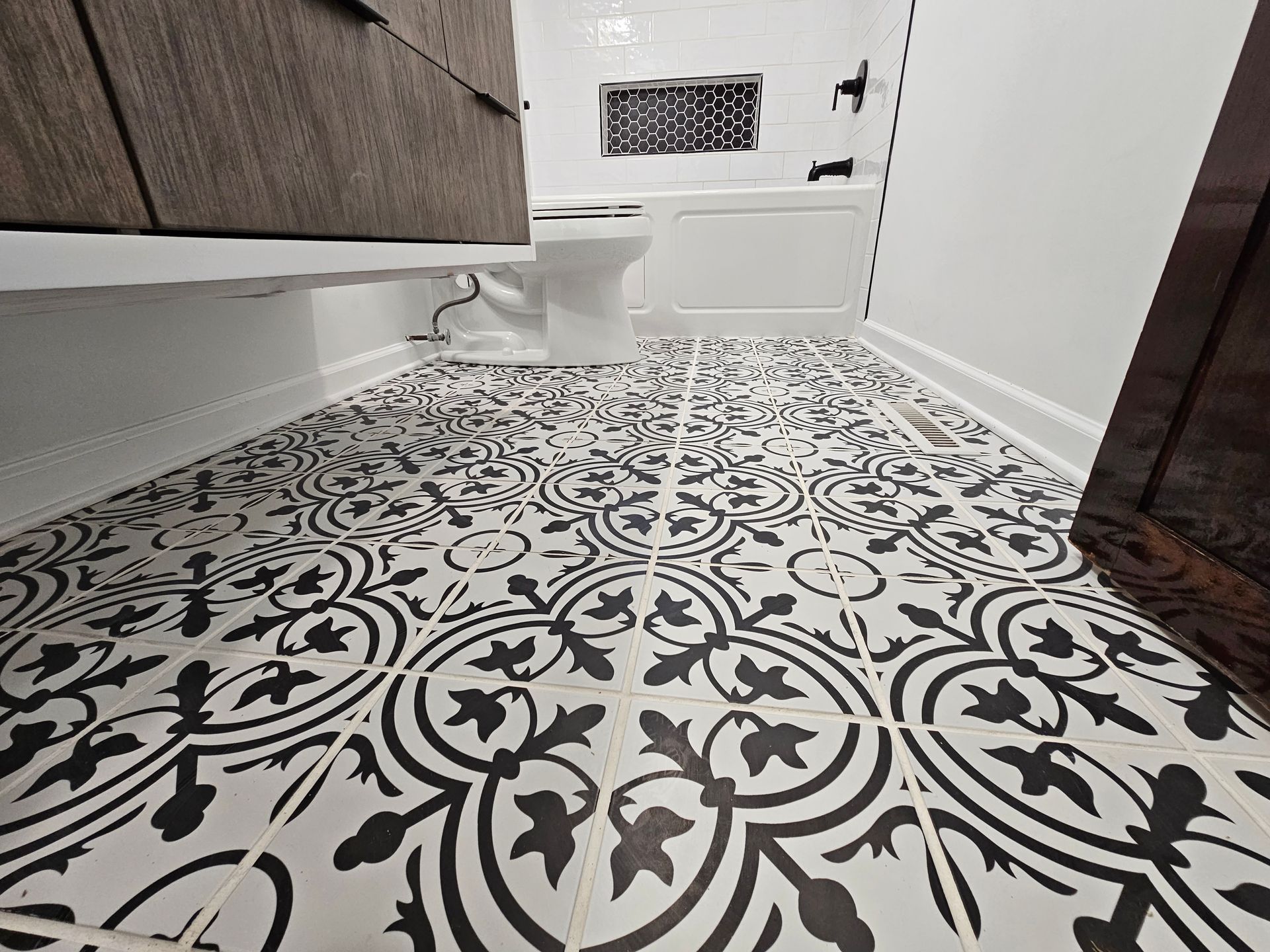Black-and-white patterned tile floor in a small bathroom or hallway, with cabinets and a wall vent.