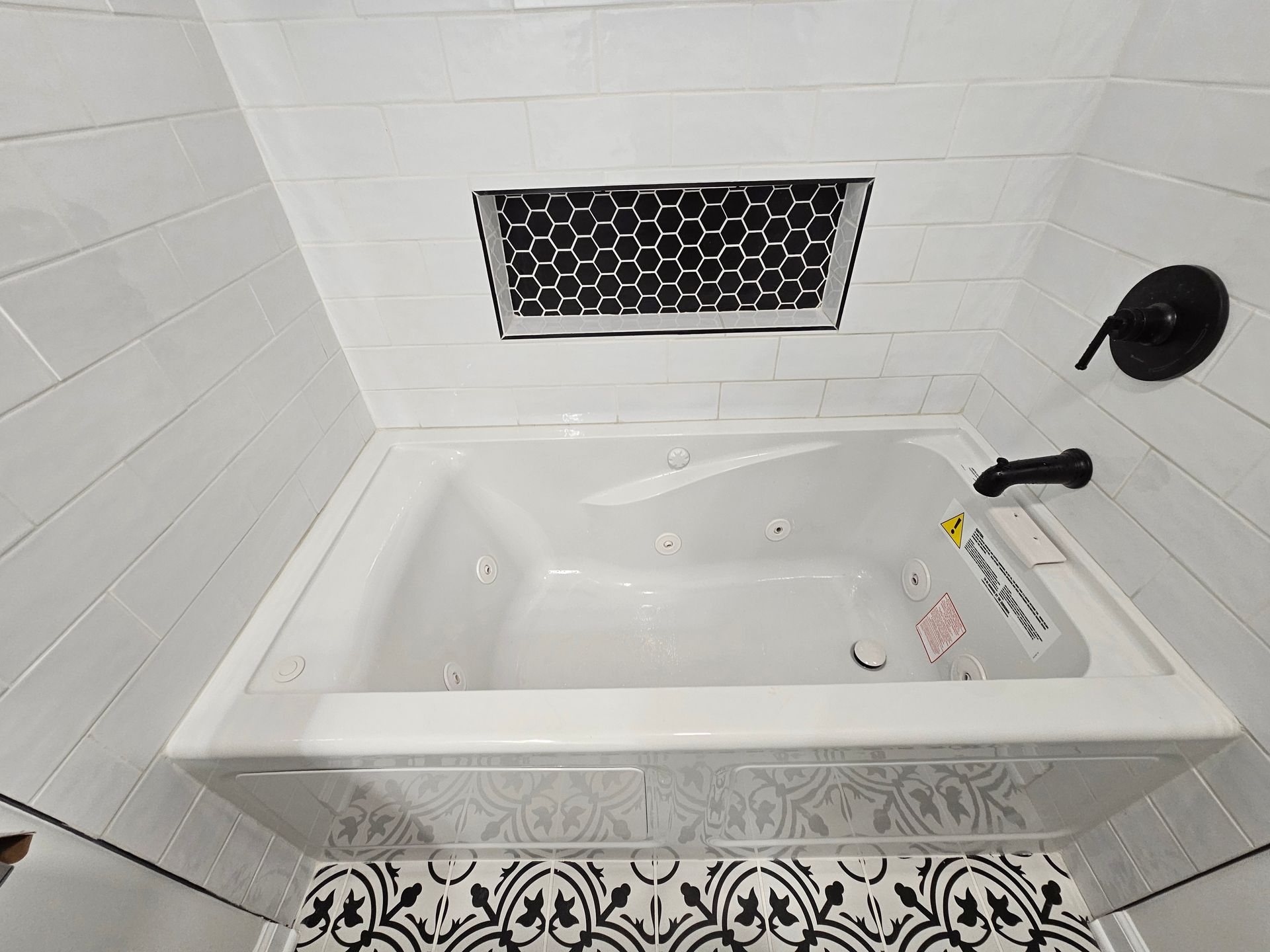 White bathtub in a tiled bathroom with a decorative vent and black faucet handle.