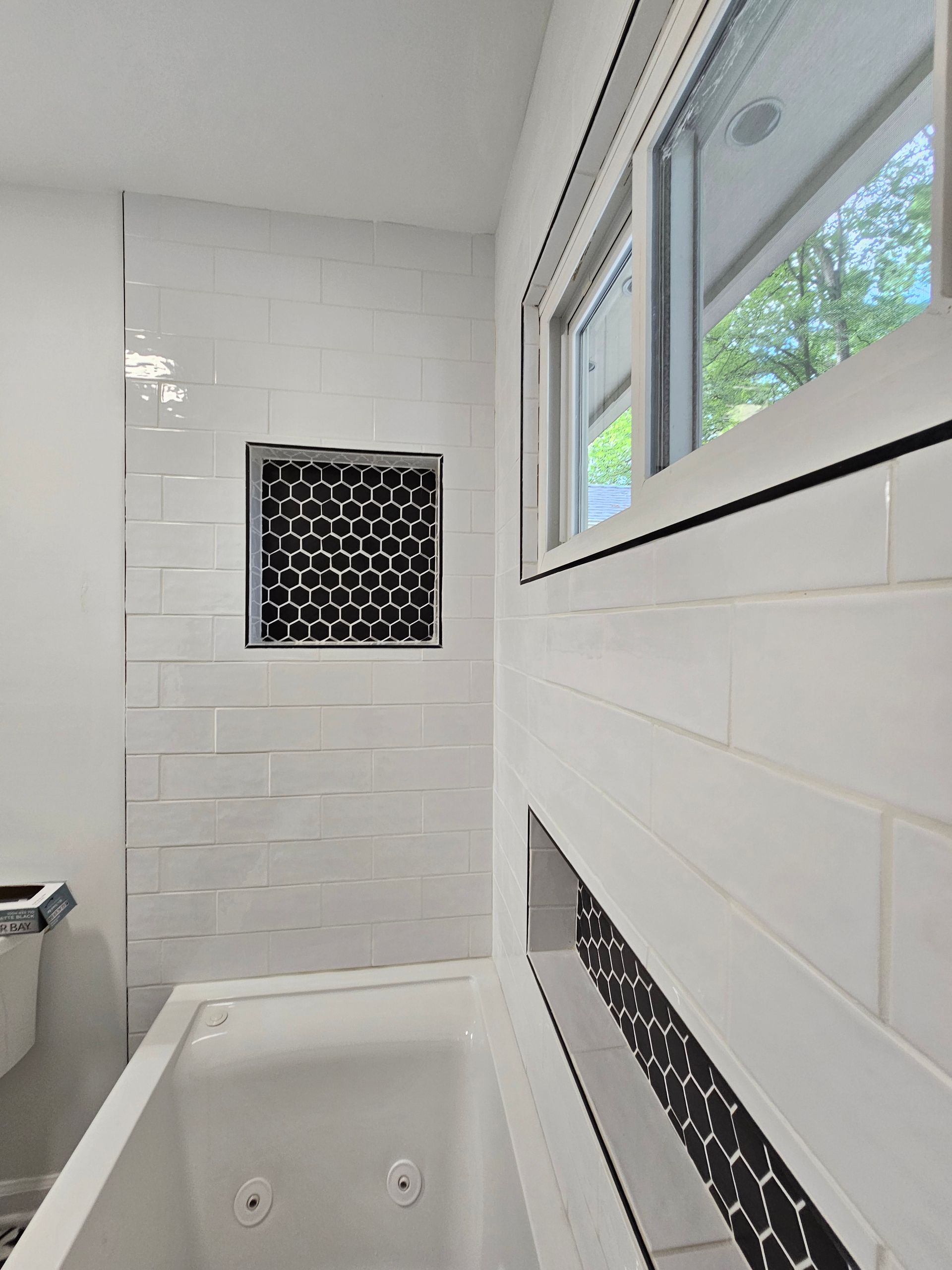 Small white bathroom with a tub, window, and black mosaic tile accent wall