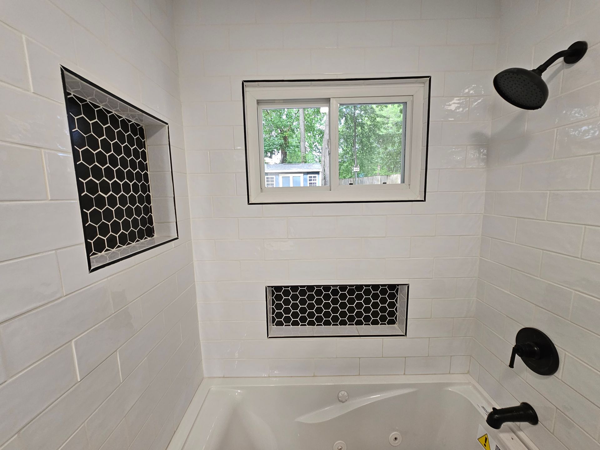 White tiled bathroom with a small window, black fixtures, and a tub-shower surround.