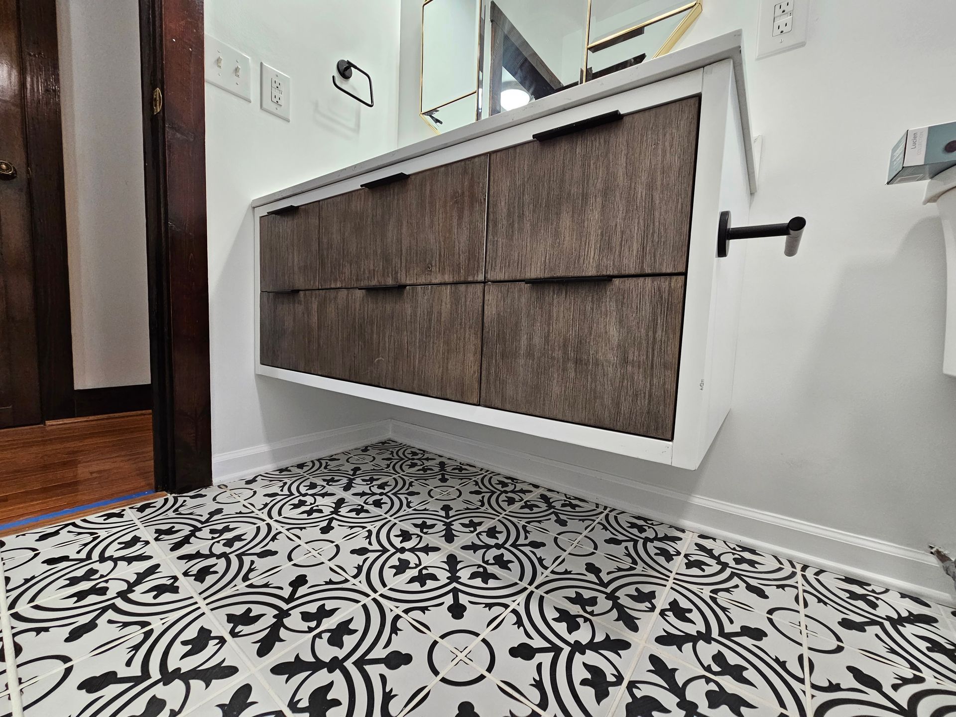 Hallway with patterned black-and-white tile floor and a tilted wall cabinet with woven brown panels
