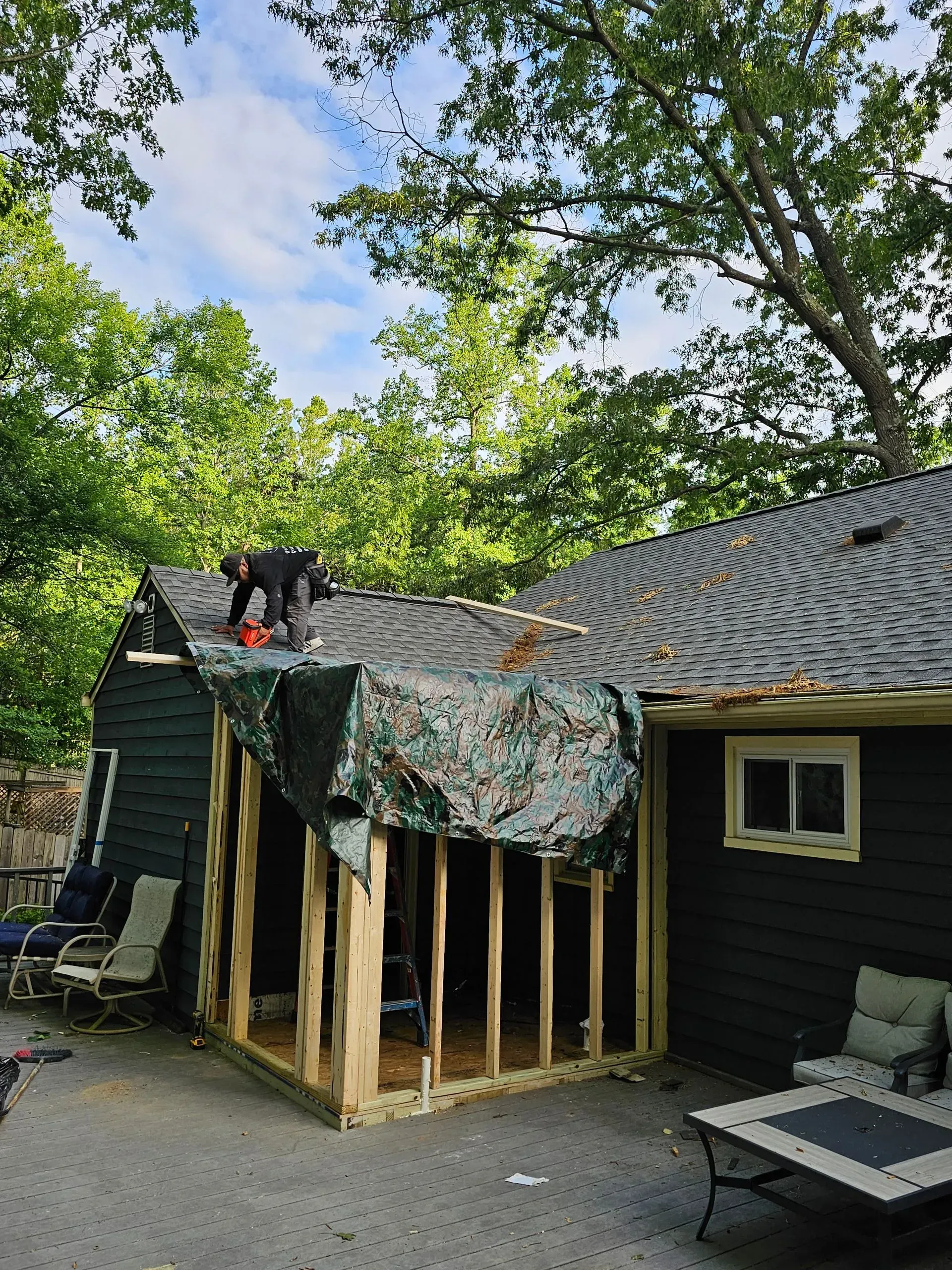 Outdoor patio covered by a partially torn camouflage tarp beside a dark cabin under trees
