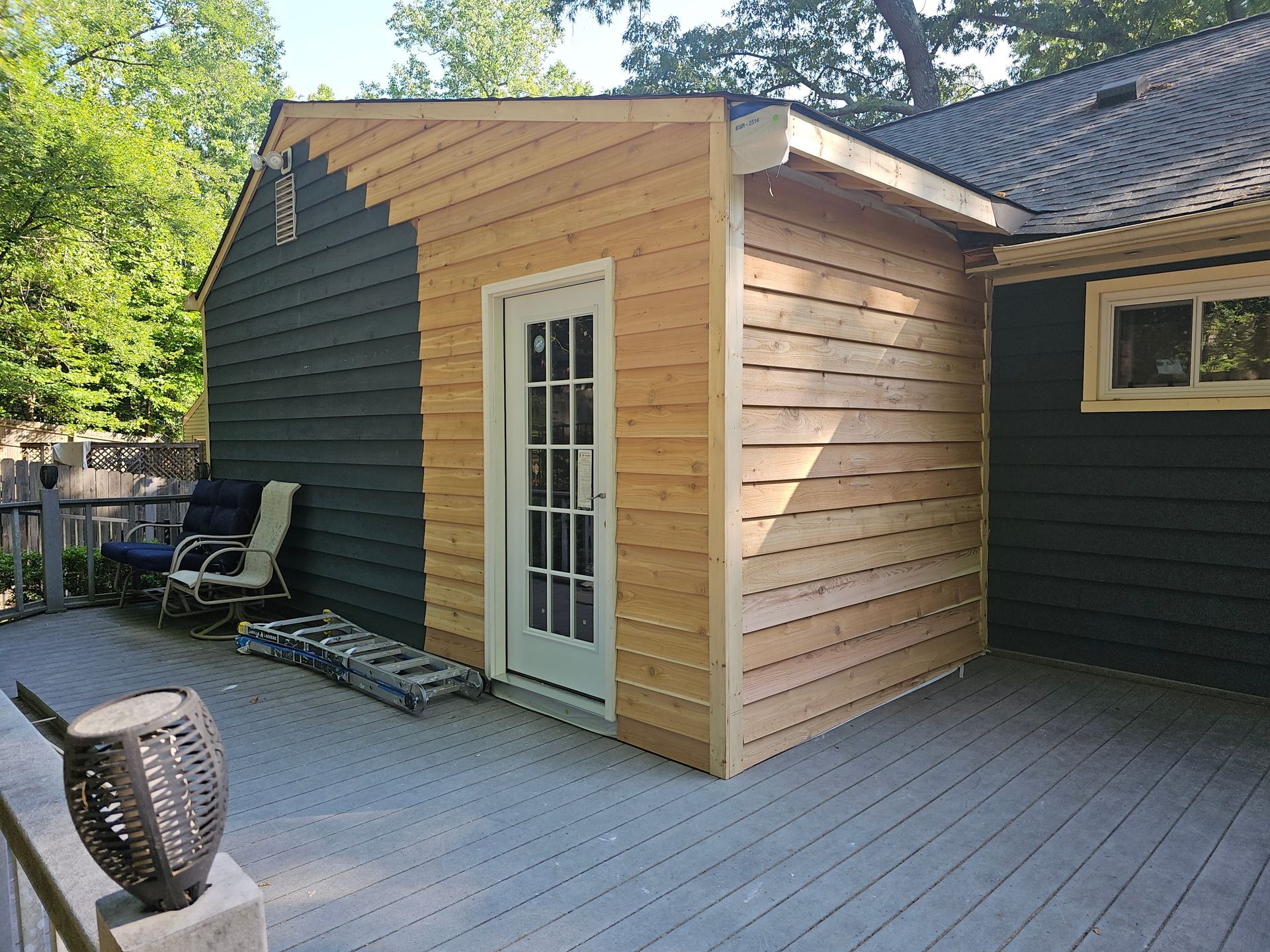 Backyard deck with a small cedar-sided shed and white French door beside a dark house wall