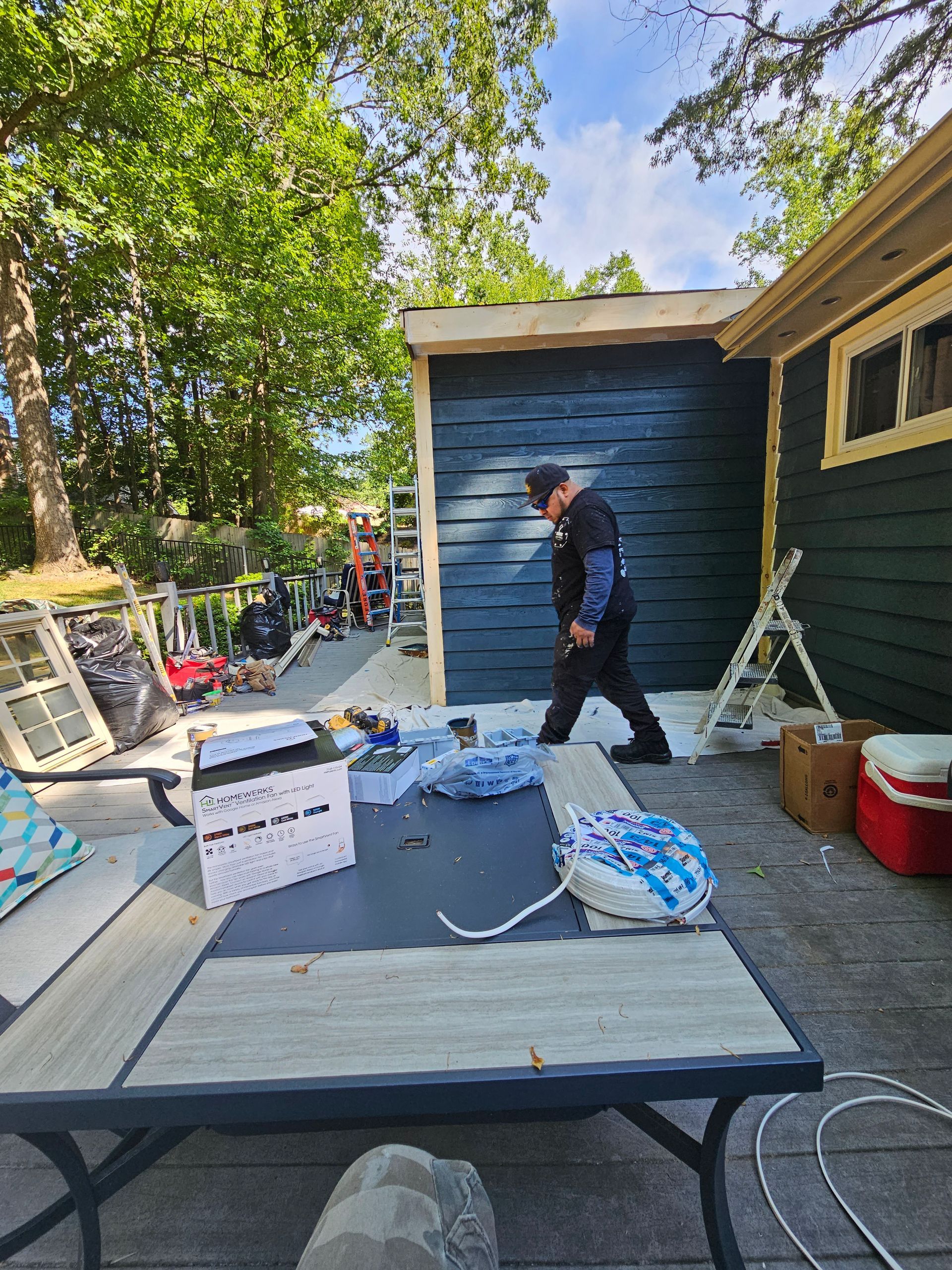 Person painting an outdoor shed in a backyard, with tools and supplies scattered nearby.