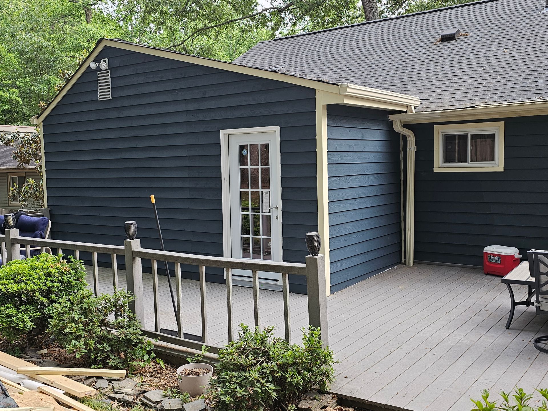 Back deck attached to a dark blue house with white railing and patio furniture