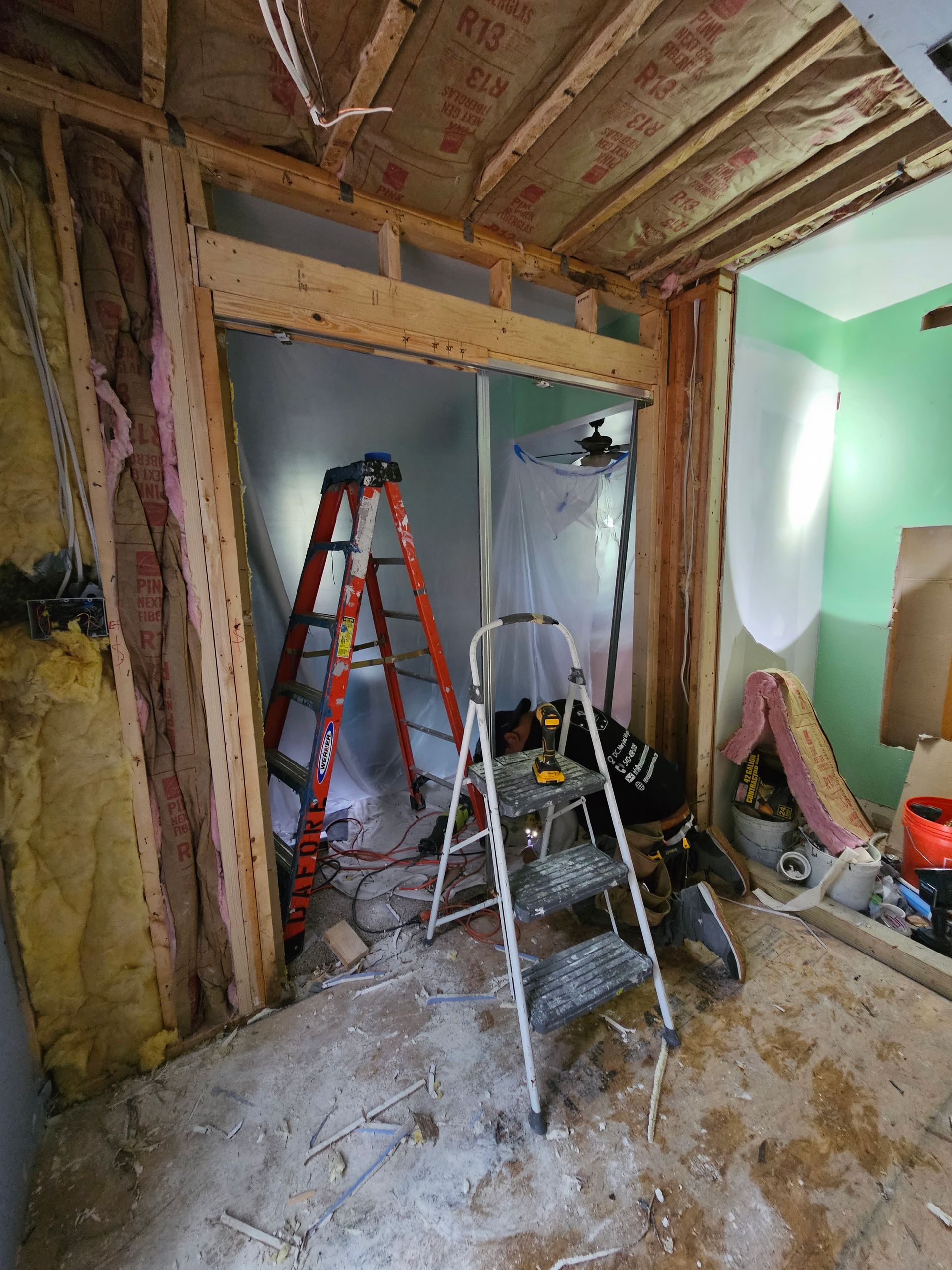 Partially renovated room with exposed studs, ladders, tools, and construction debris on the floor