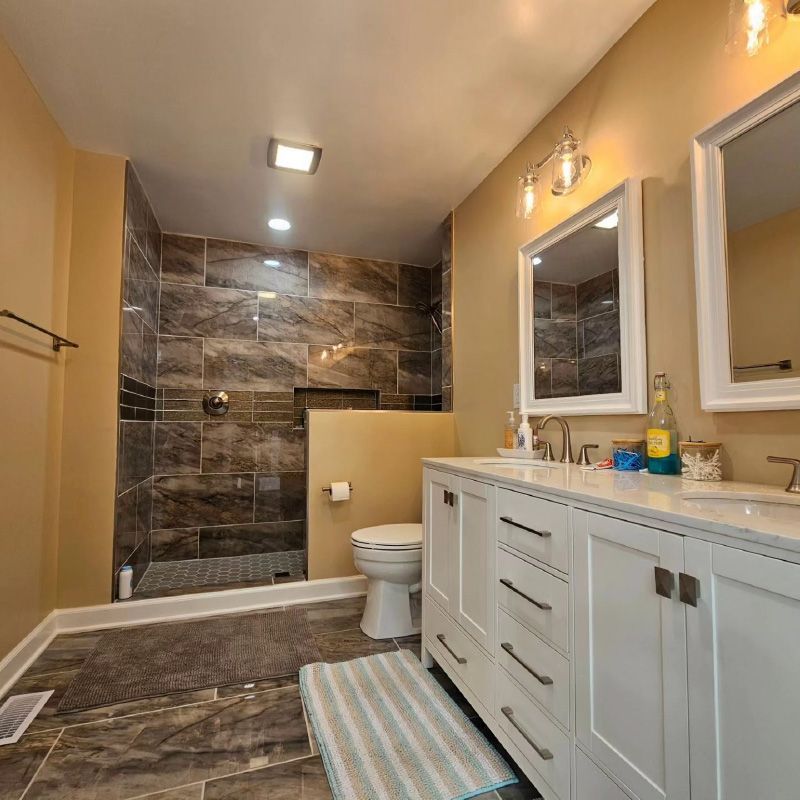 Modern bathroom with marble shower, double vanity, toilet, and striped rug