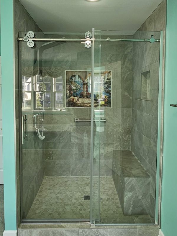 Glass-enclosed shower with gray tile walls, sliding doors, and a built-in bench