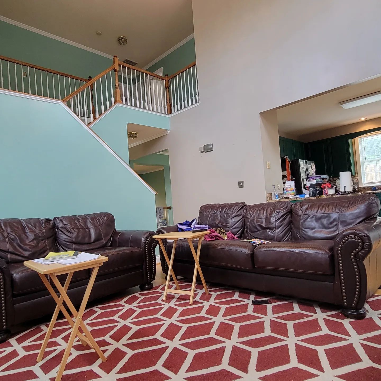 Living room with brown leather sofas, red patterned rug, and staircase in the background