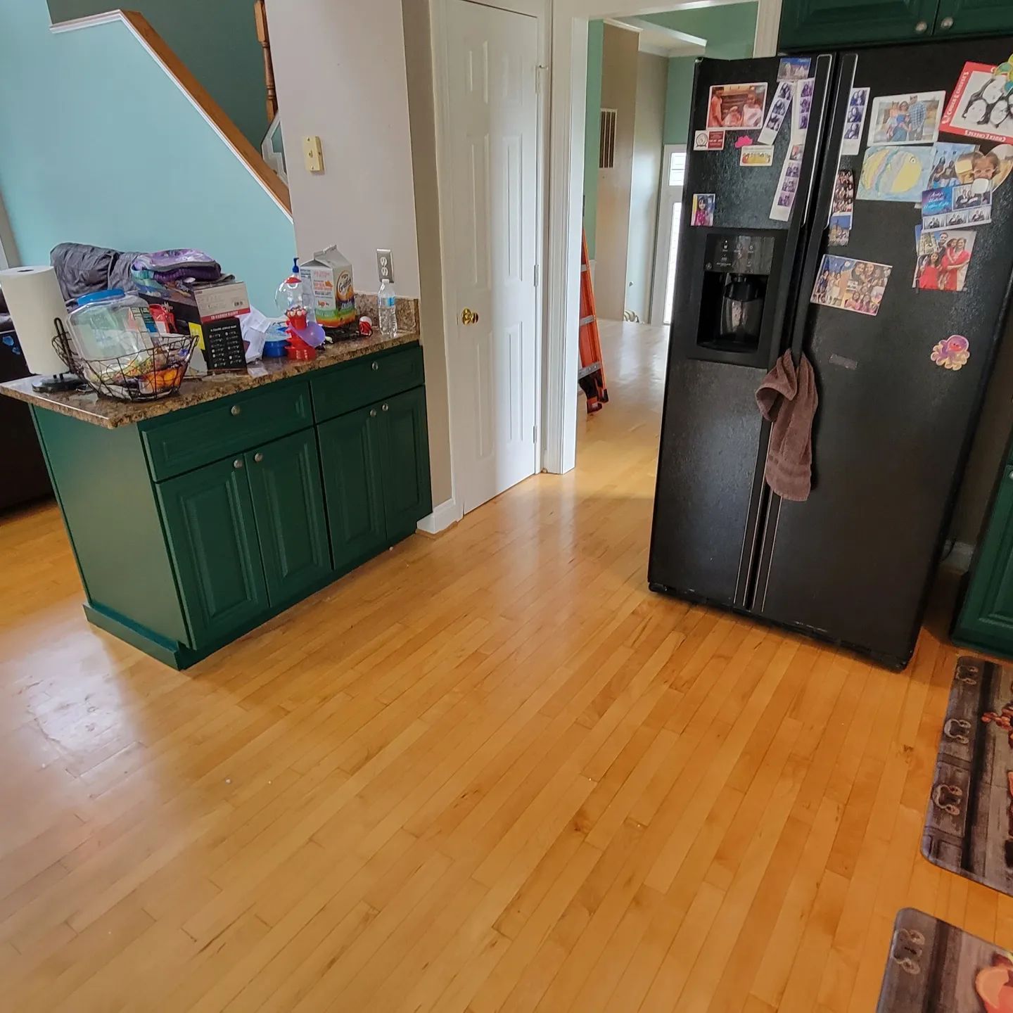 Kitchen with wood floor, green cabinet, and black refrigerator covered in magnets and photos.