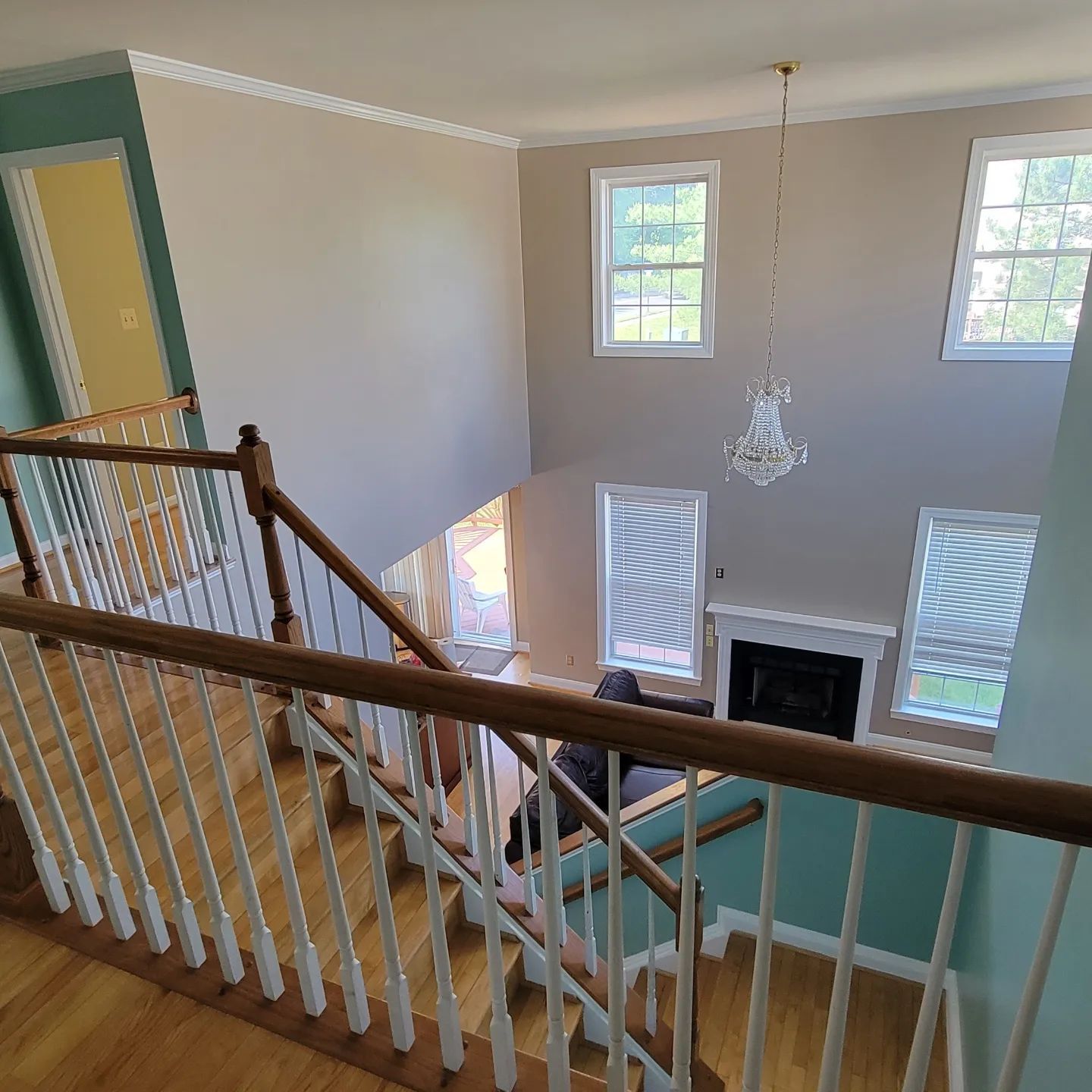 Upper landing view over staircase into bright foyer with chandelier, windows, and fireplace
