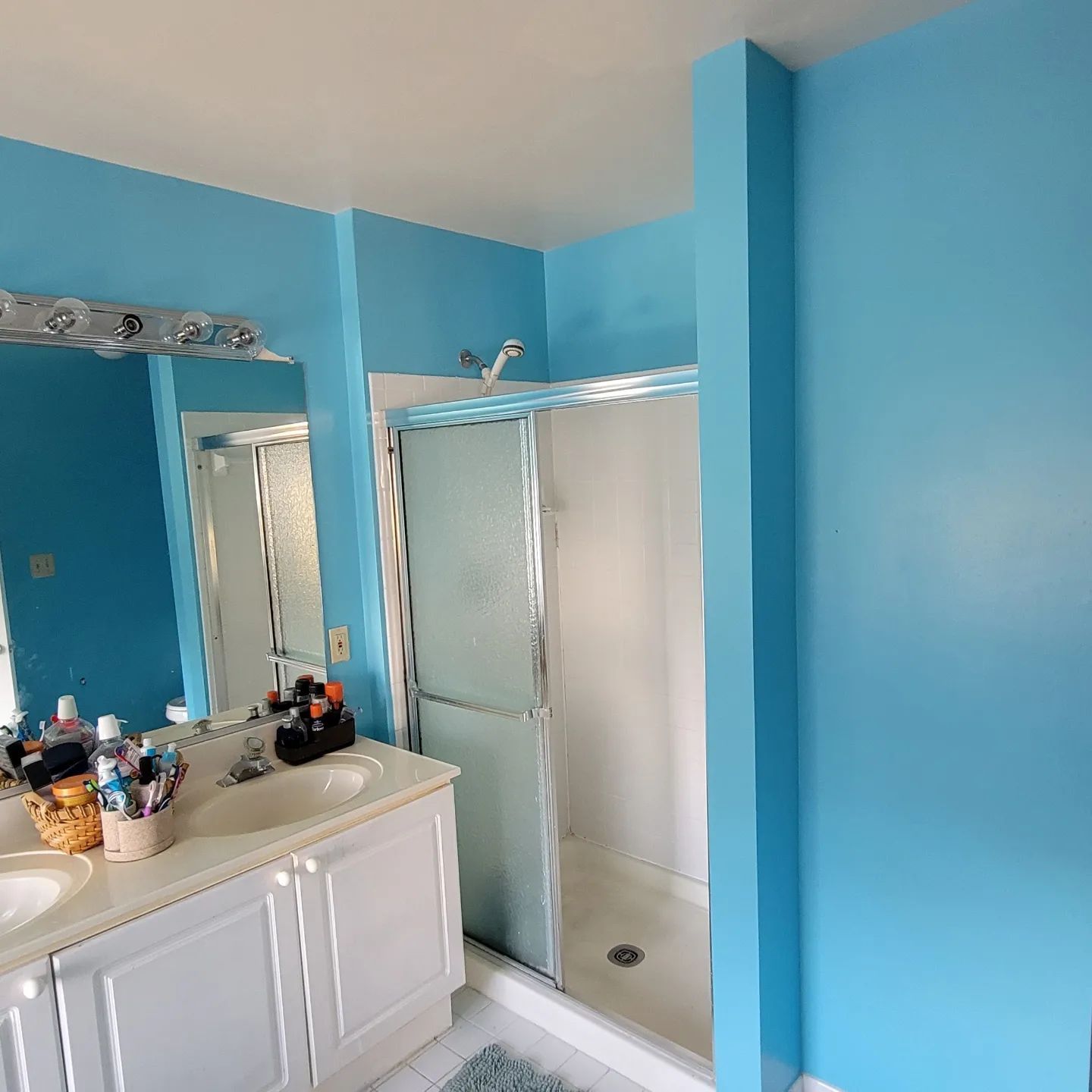 Bright blue bathroom with vanity, large mirror, and glass shower stall.