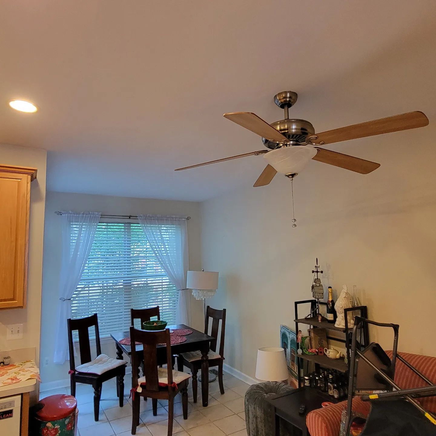 Dining area with table and chairs, ceiling fan, window blinds, and a shelf with decor and storage bins.