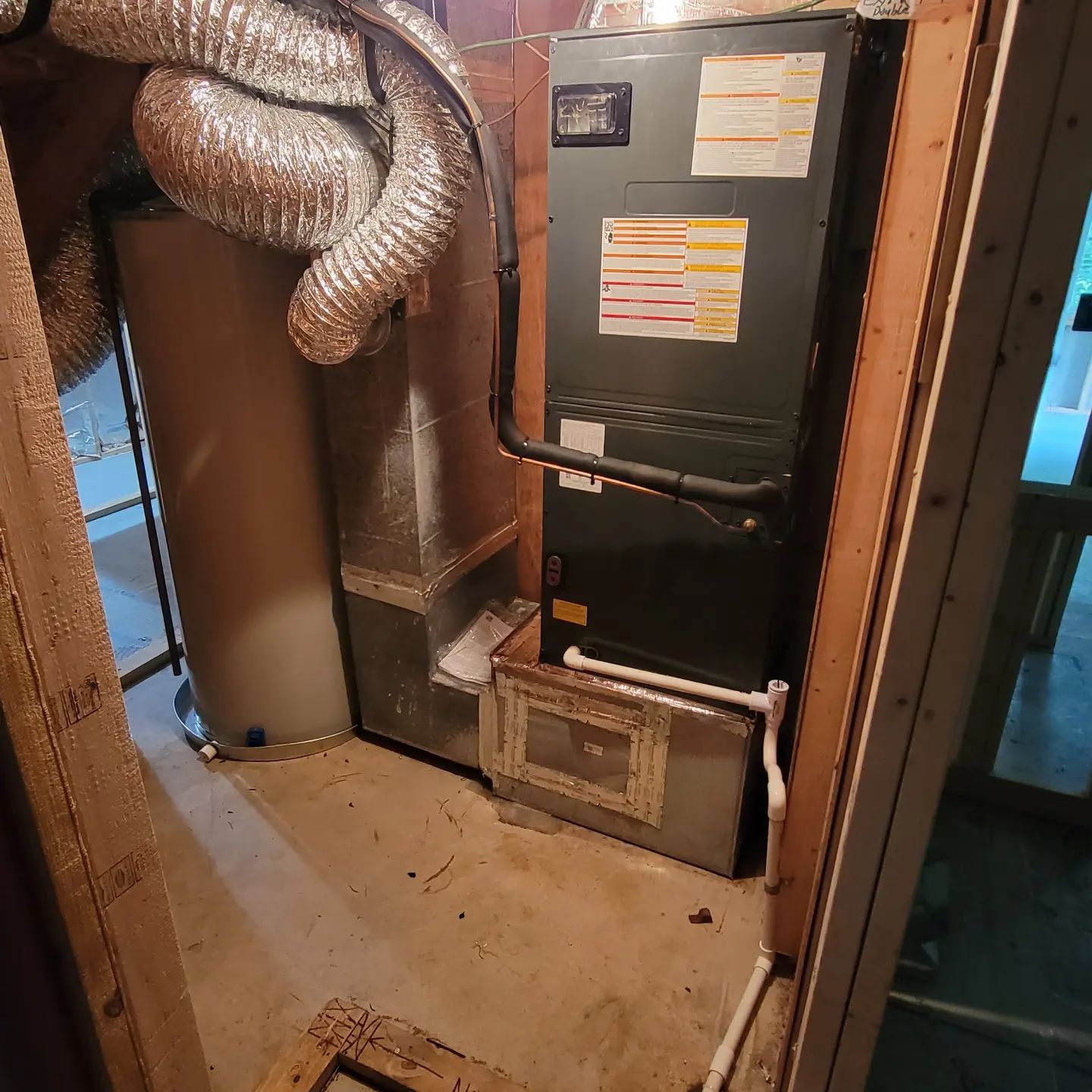 Basement HVAC furnace beside ductwork and a water heater in a utility closet