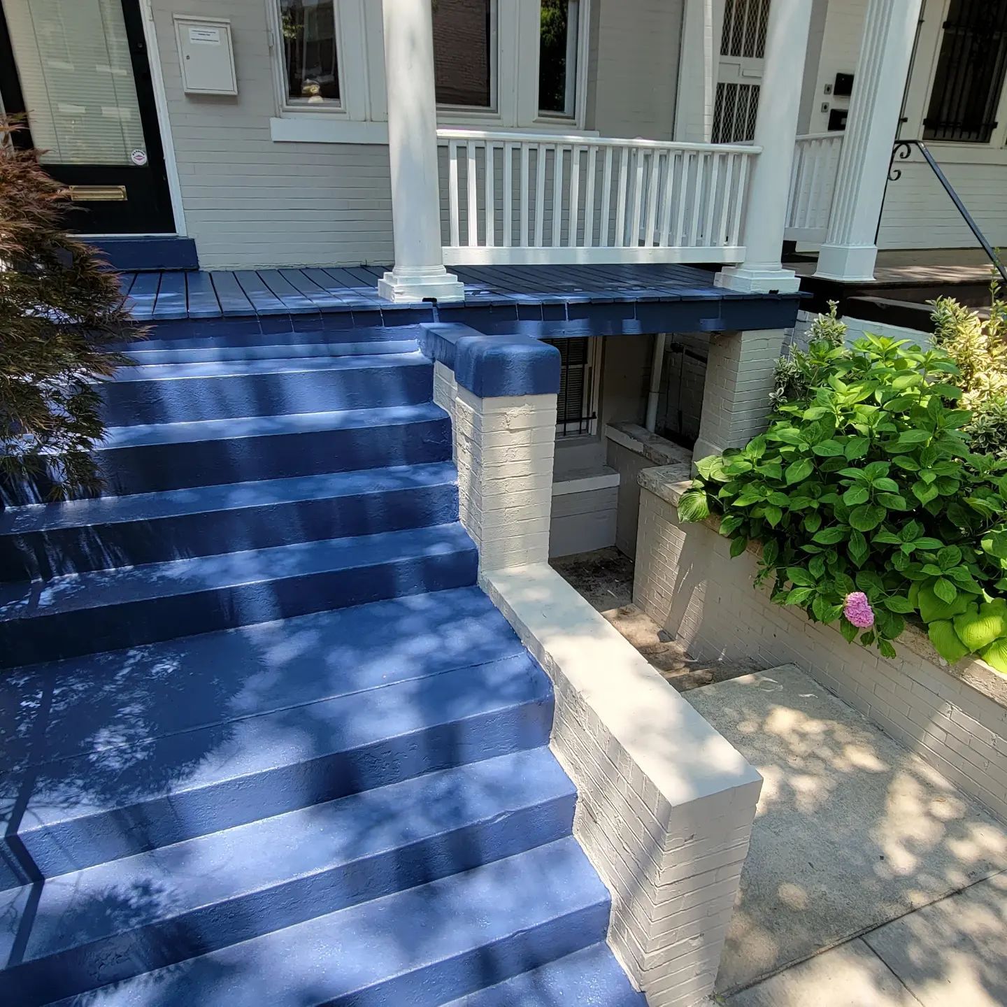 Blue-painted front steps leading to a white porch with columns and a shrub beside a walkway