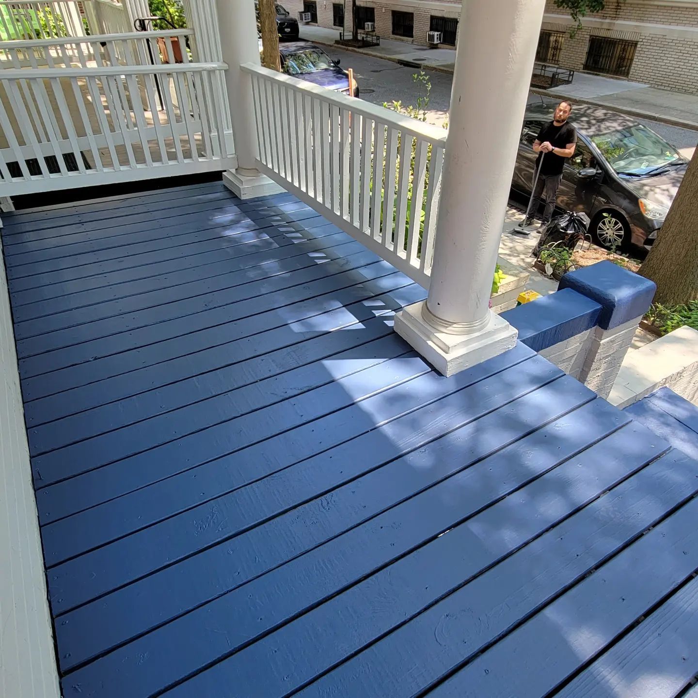 Blue-painted porch floor with white railings and columns overlooking a street below
