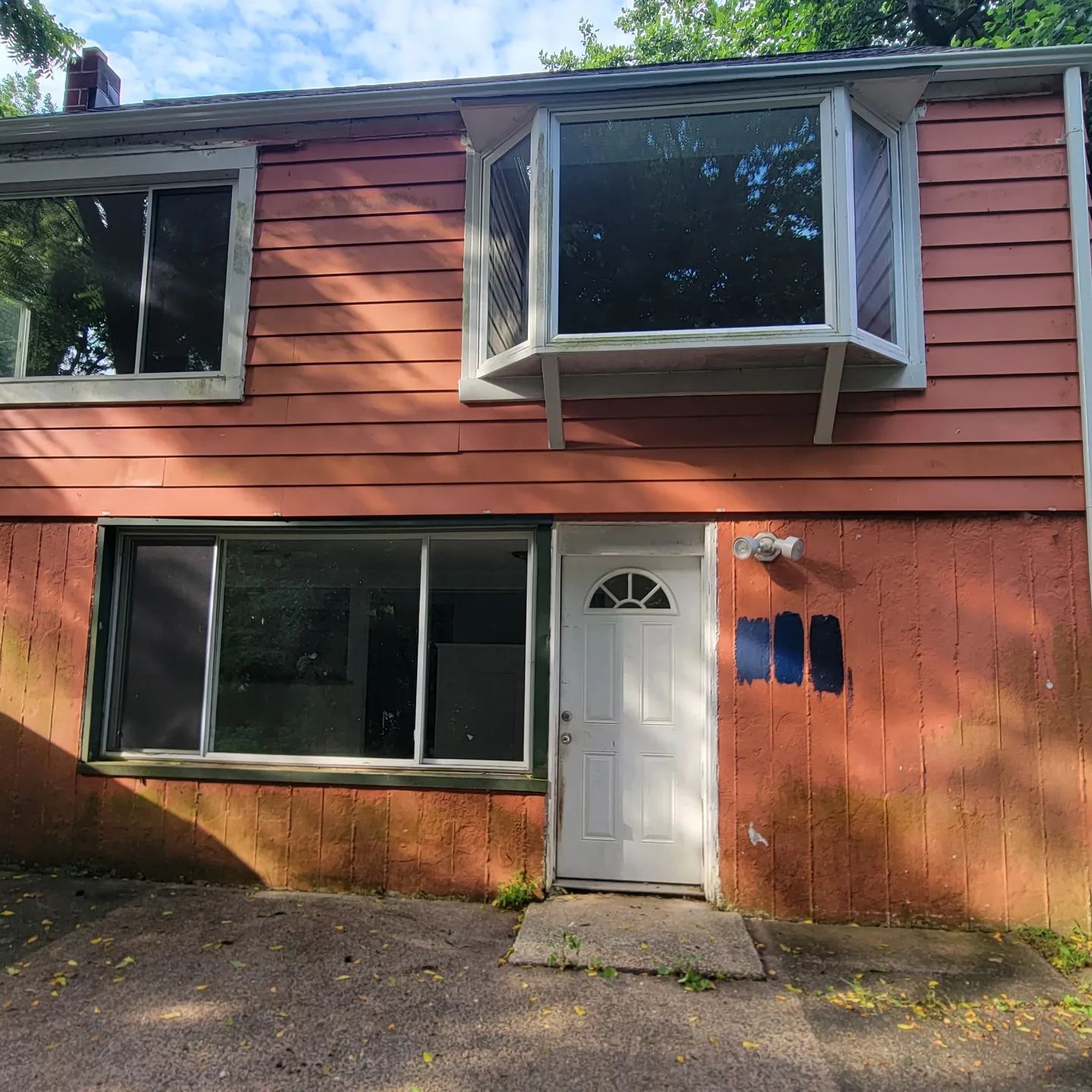 Two-story red house facade with a white door, large windows, and a small concrete stoop.