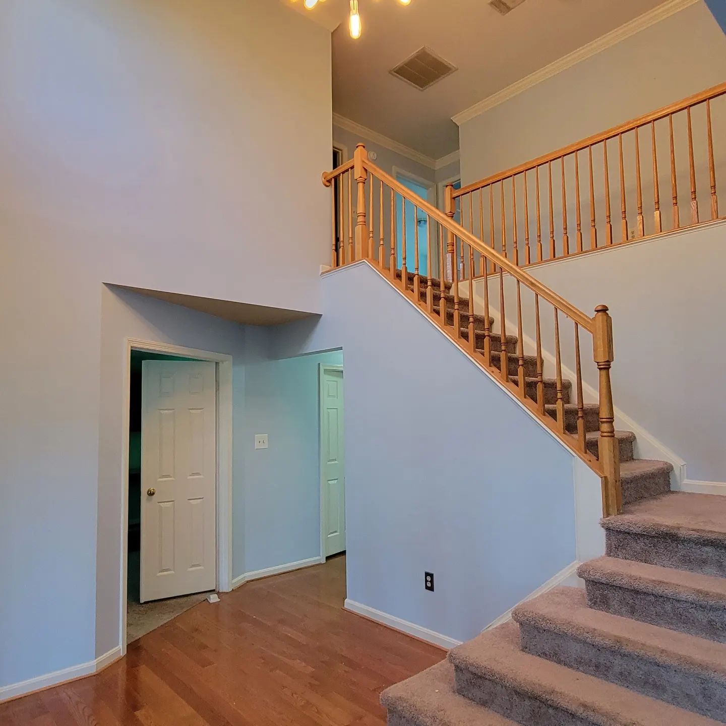 Empty foyer with staircase, wood floor, and blue walls beneath a tall ceiling