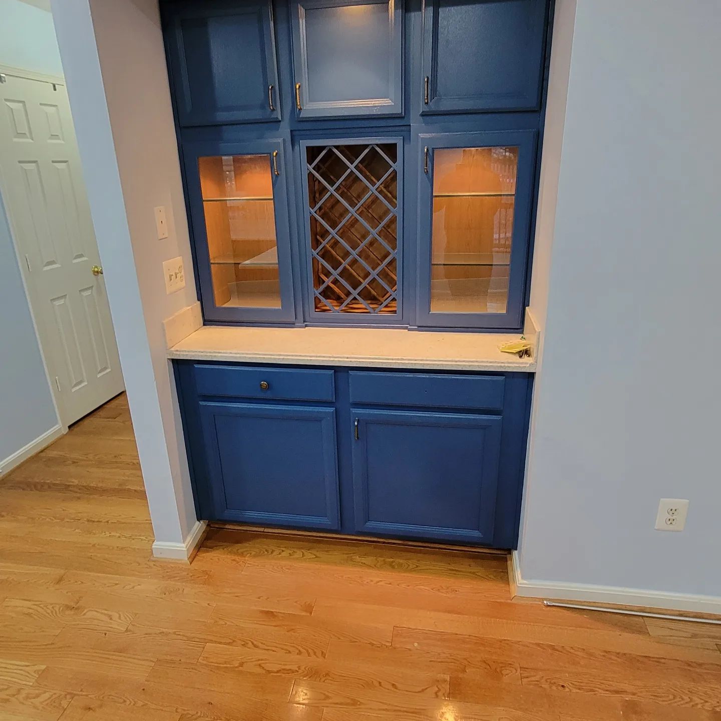 Blue built-in cabinet with glass-front upper doors and wood countertop in a room with hardwood floors.