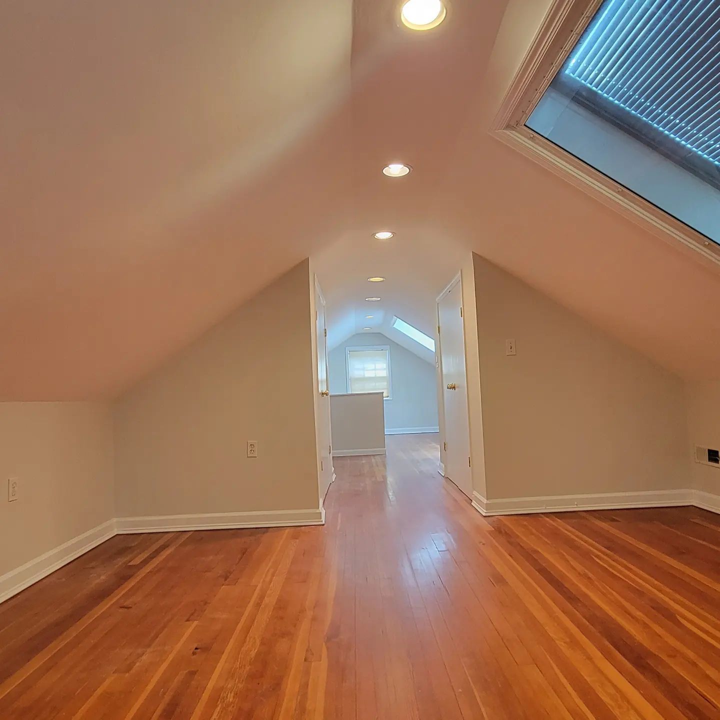 Empty attic room with sloped ceilings, hardwood floor, and skylights