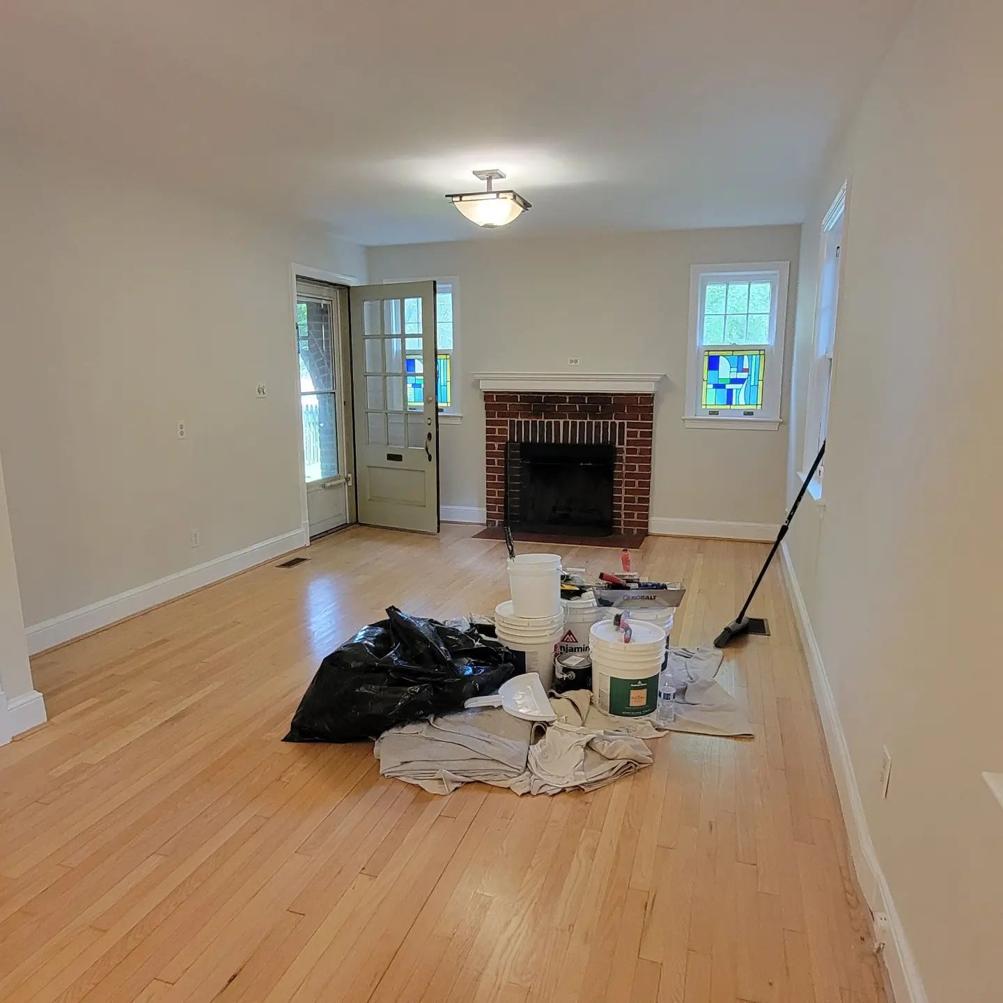 Vacant living room with hardwood floors, fireplace, and cleaning supplies piled in the center