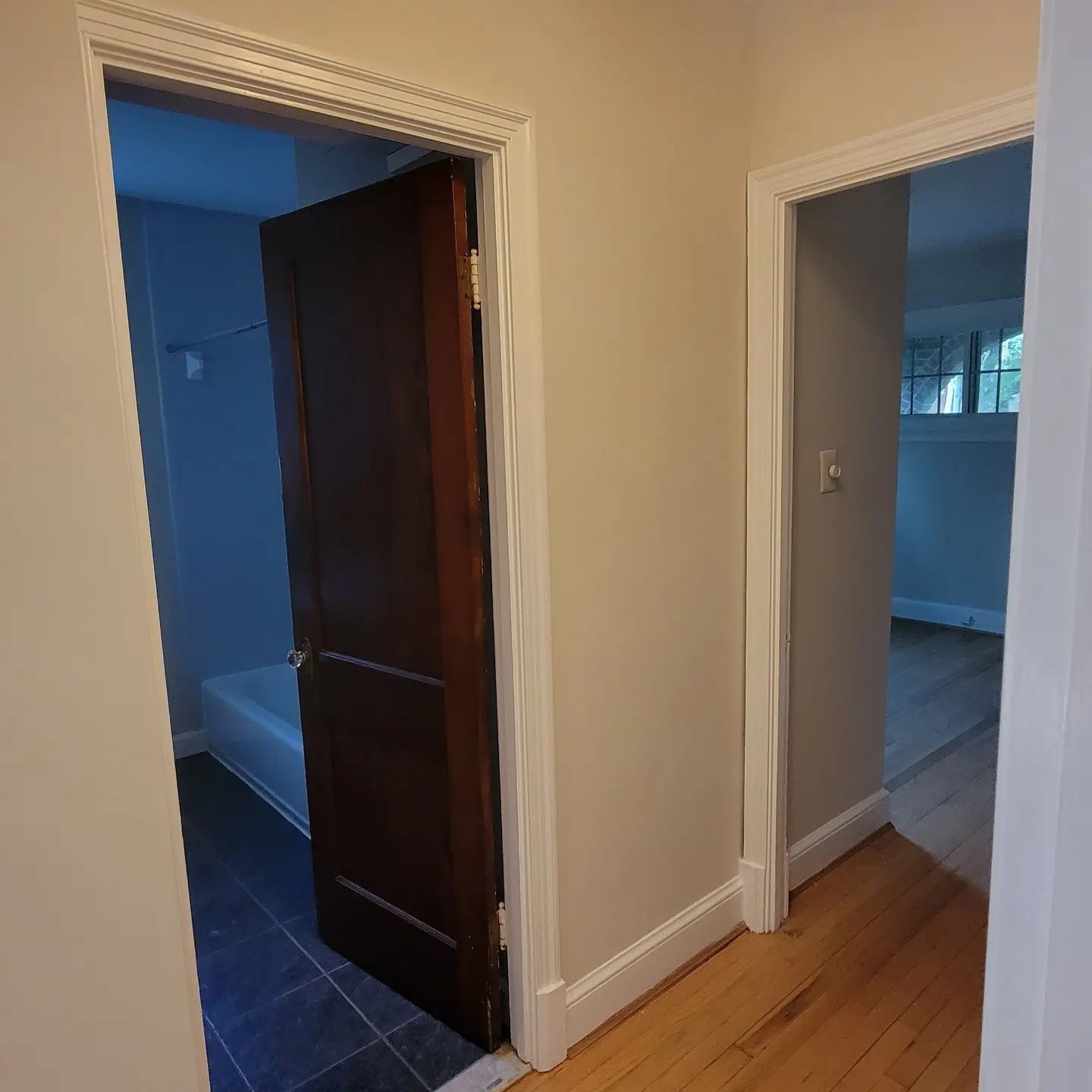 Hallway with two open doorways, showing a dark blue room on the left and a bright room on the right.