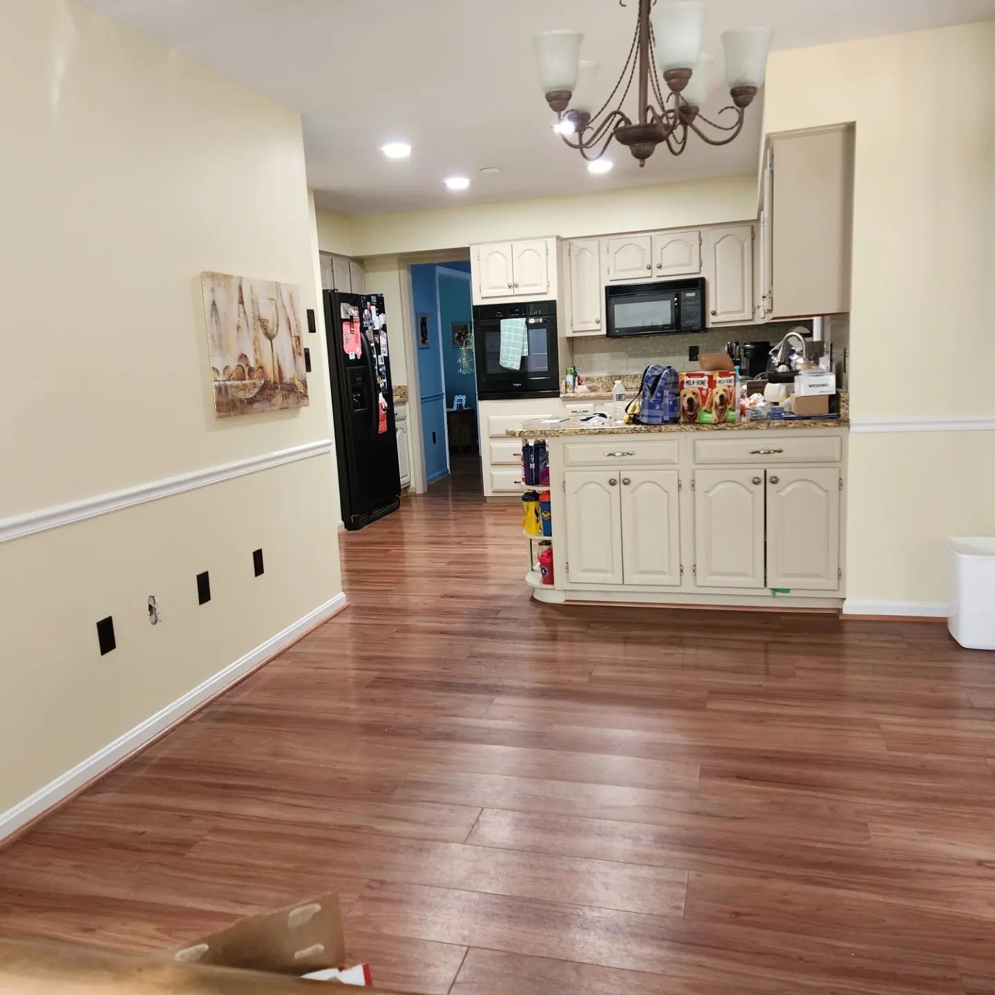 Open kitchen and dining area with hardwood floors, white cabinets, and a chandelier.