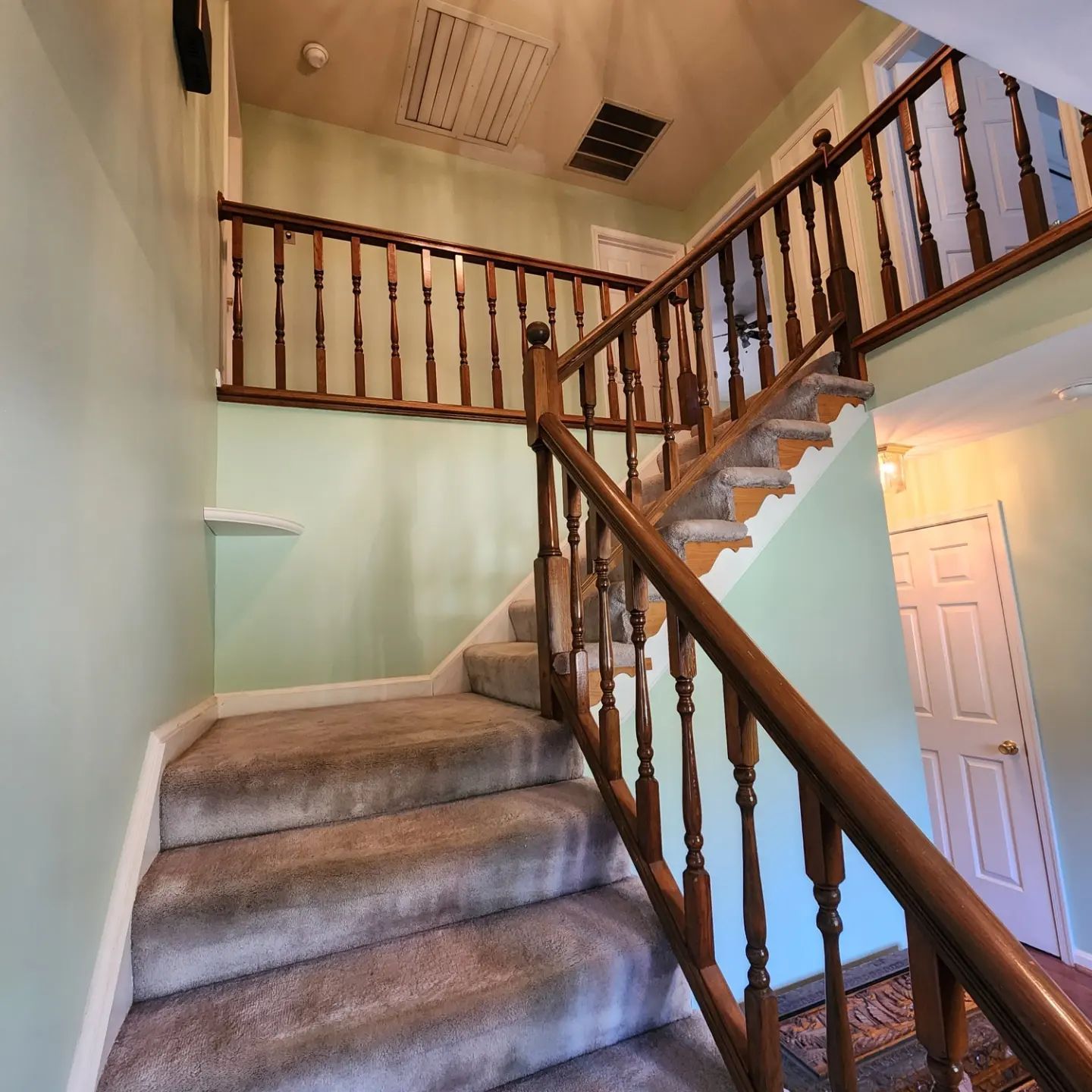 Carpeted staircase with wooden railing leading to an upper landing in a home foyer.