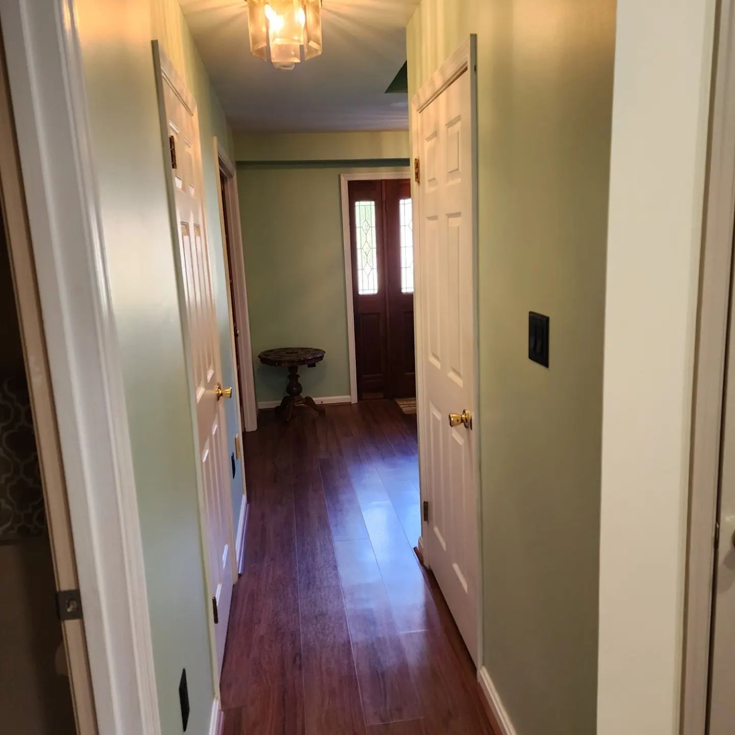 Narrow hallway with green walls, white doors, hardwood floor, and a front door at the end.