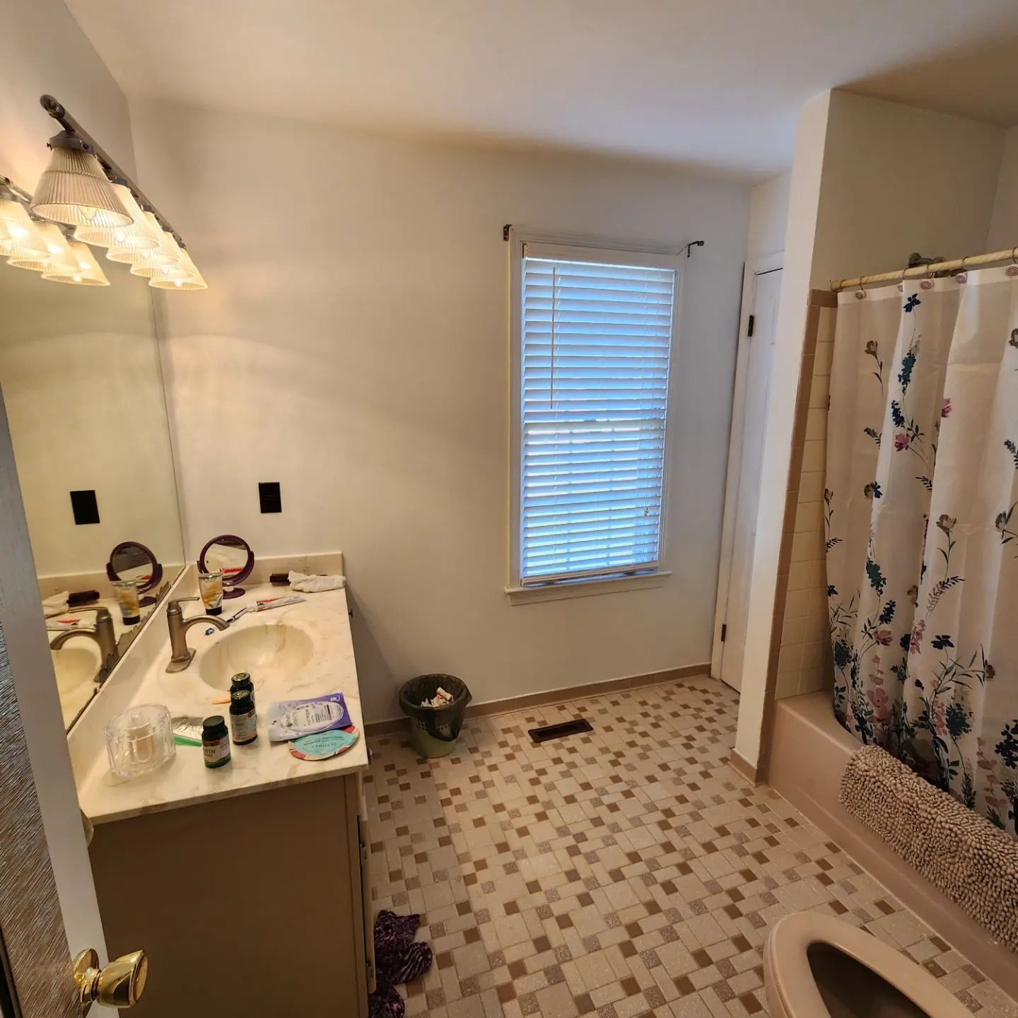 Small bathroom with vanity, mirror lights, shower curtain, window, and tiled floor.