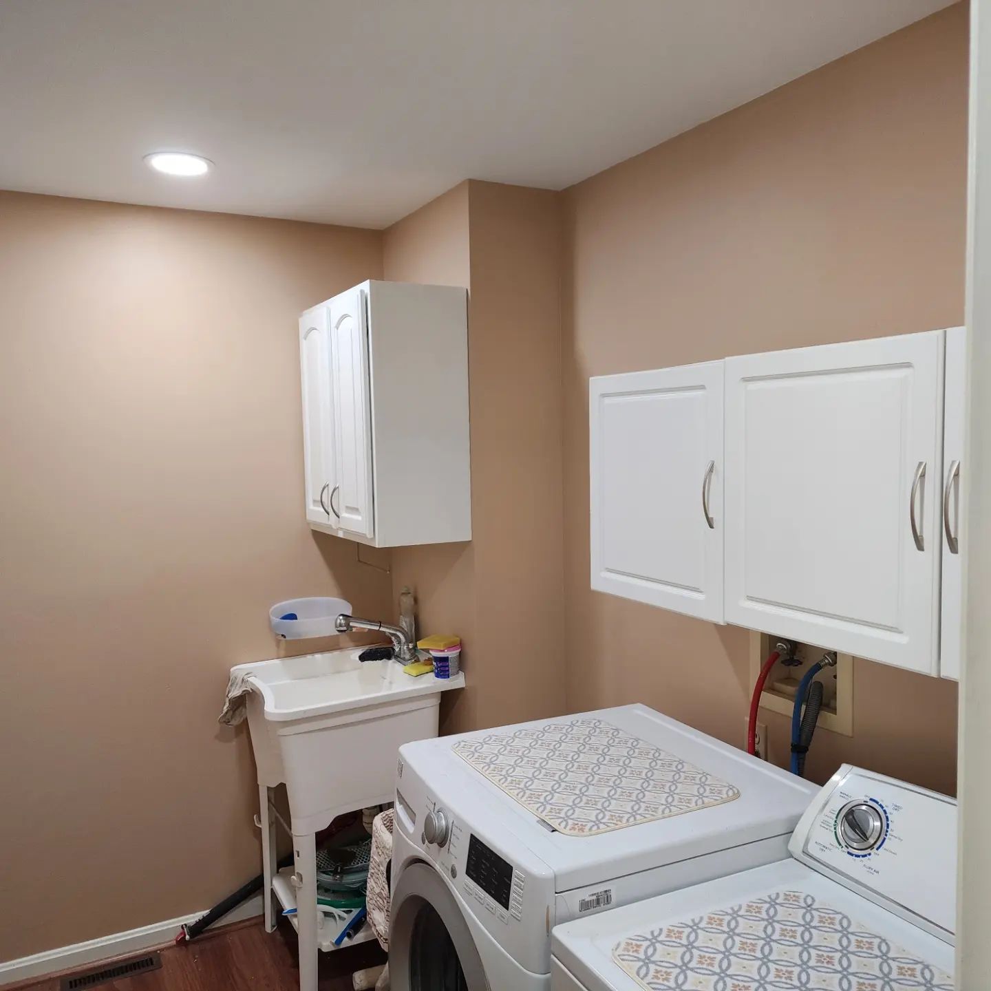 Laundry room with tan walls, white cabinets, utility sink, and a washer and dryer.