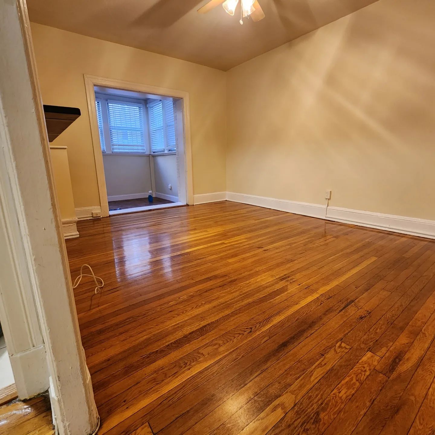 Empty room with hardwood floors, beige walls, and a window with blinds.