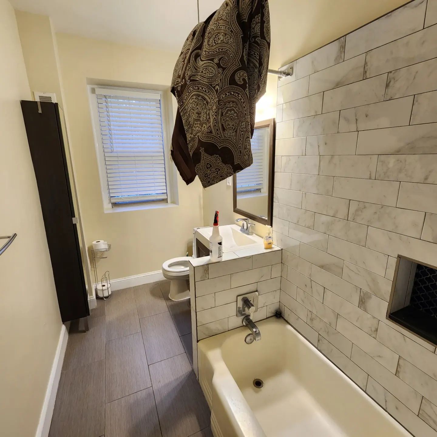 Narrow bathroom with a bathtub, toilet, sink, white tile wall, and a robe hanging from the ceiling.