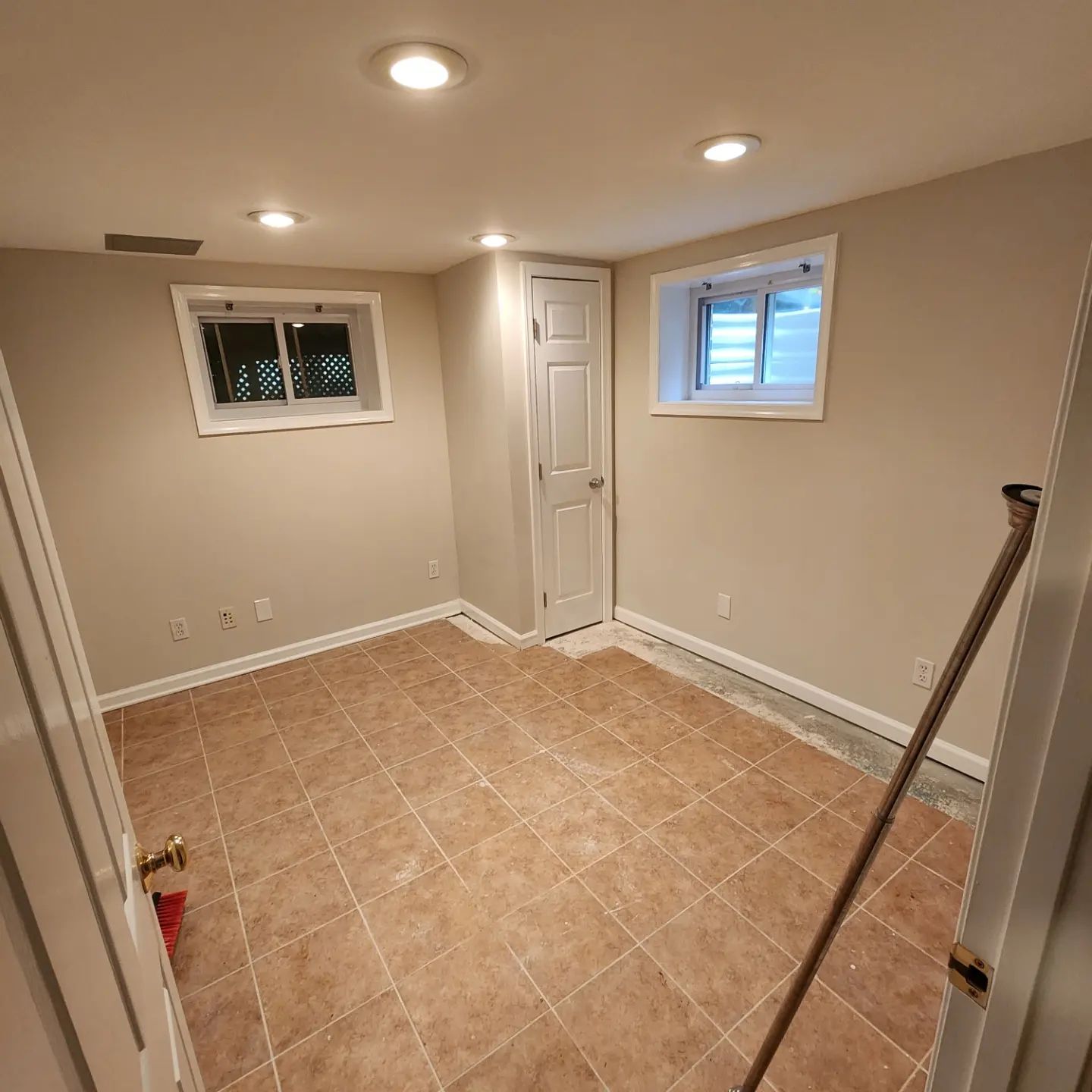 Empty beige room with tiled floor, recessed lights, small windows, and a closed door
