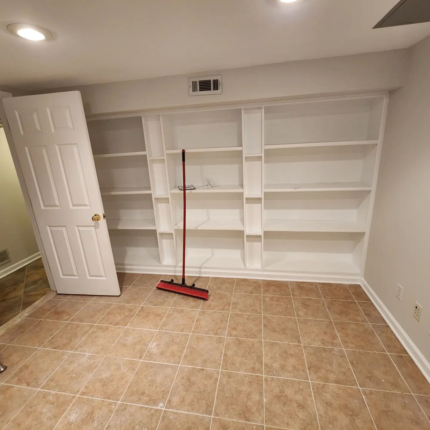 Empty white built-in shelves in a tiled room with a red broom and open door.