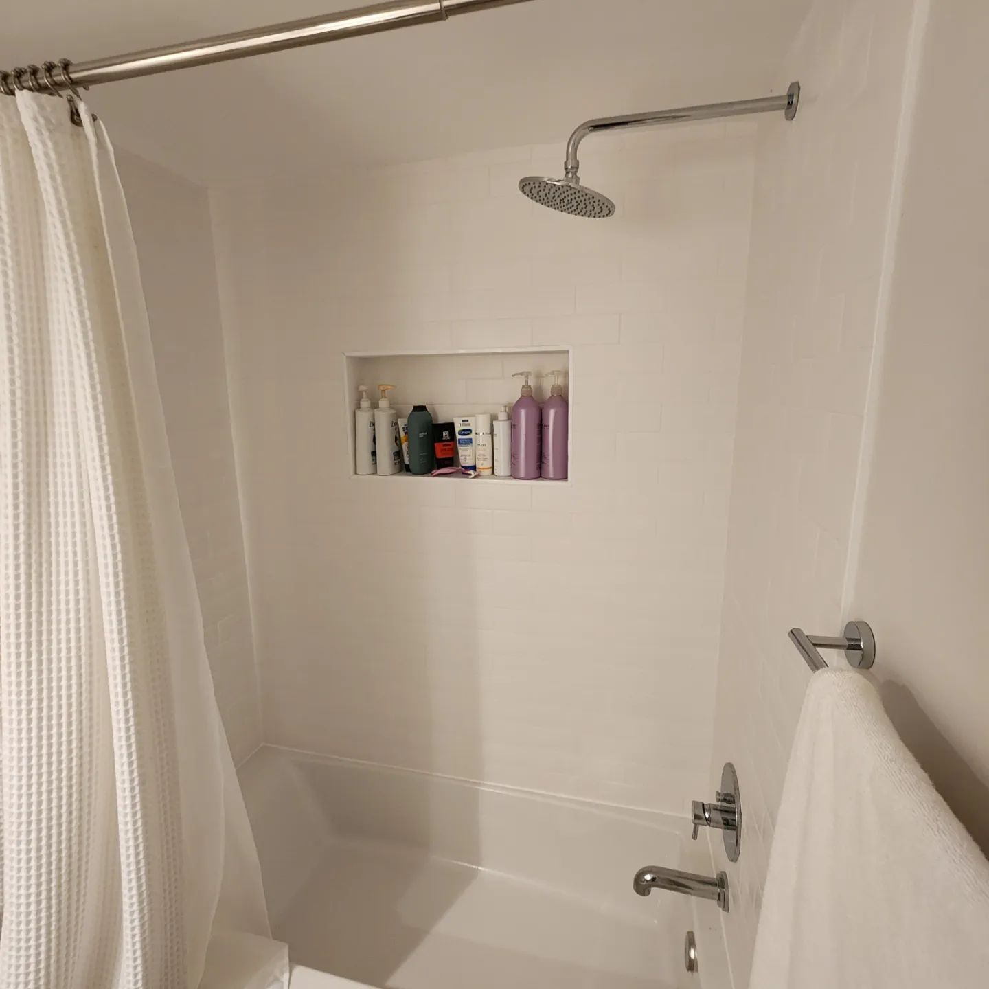 Clean white bathtub shower with built-in niche holding toiletries and a towel on the rack