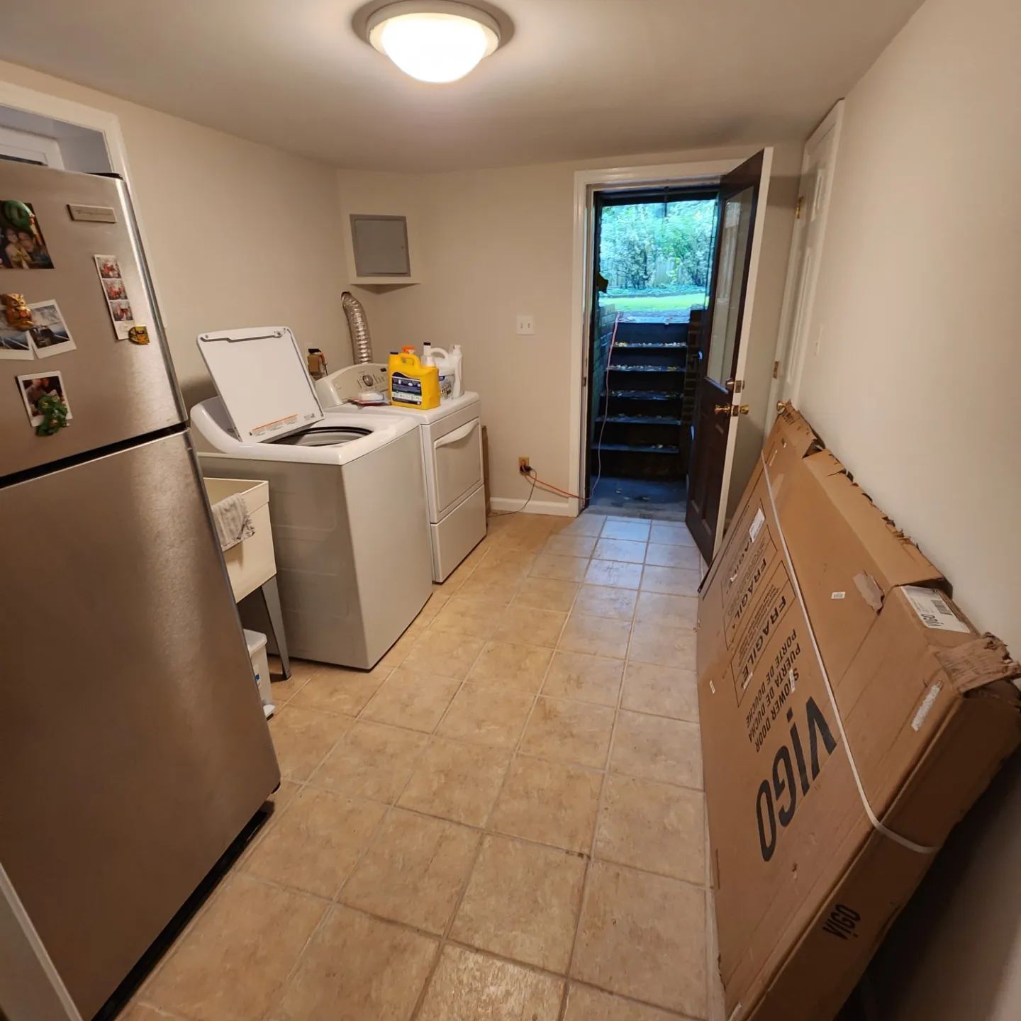 Small kitchen with washer, dryer, fridge, and a large cardboard box leaning against the wall.