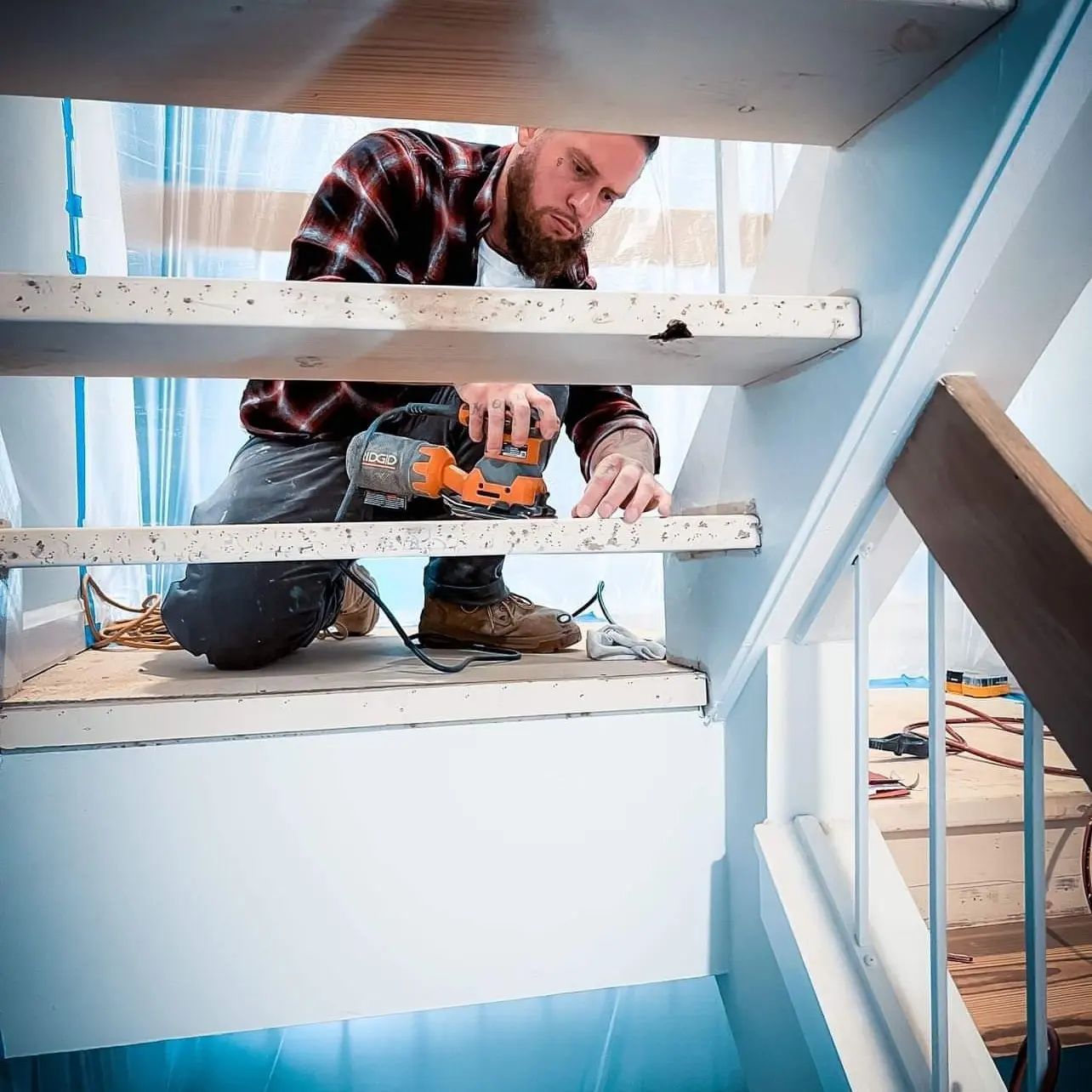 Worker using a power drill while kneeling on white stairs inside a house