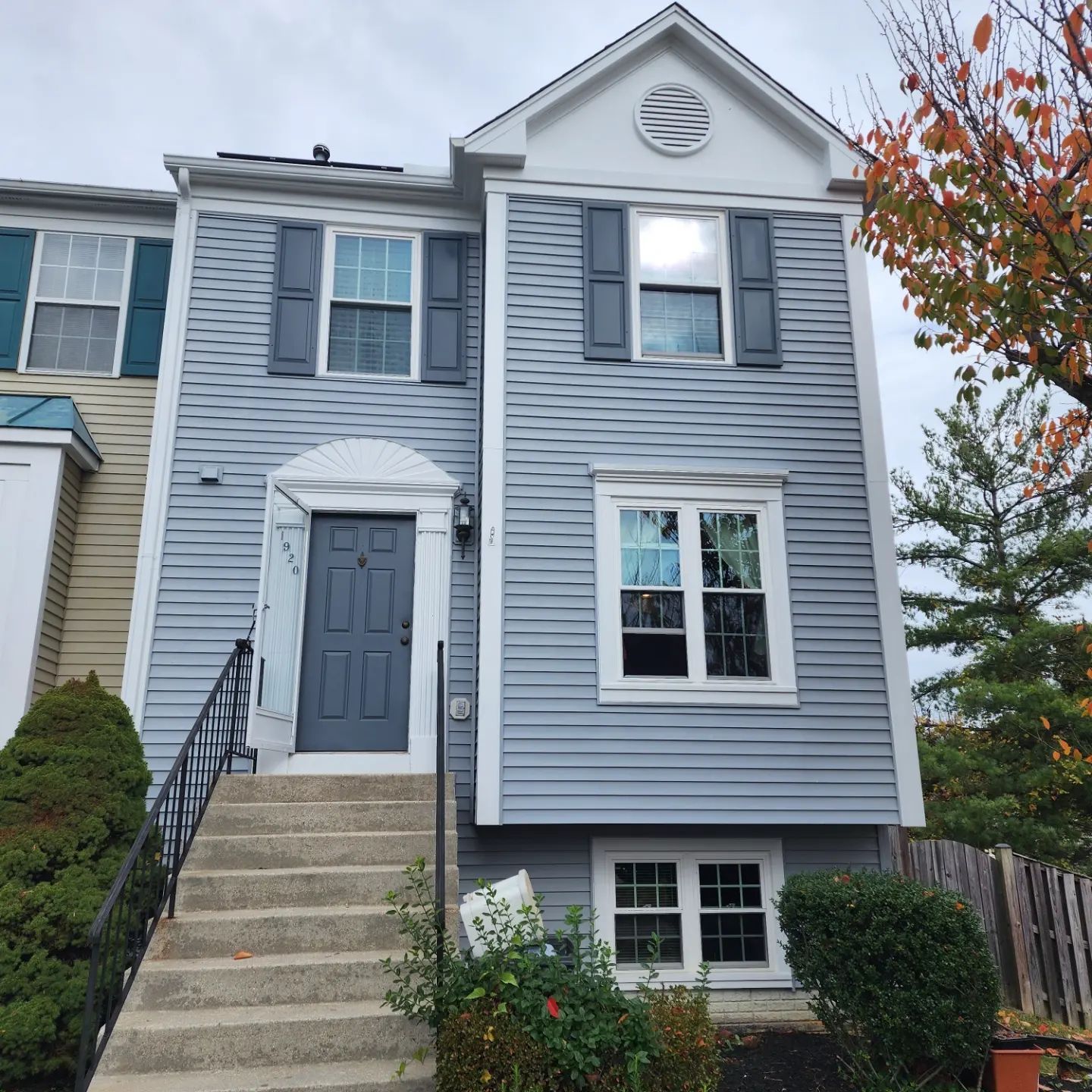 Gray two-story townhouse with front steps, blue shutters, and a small front yard in autumn.