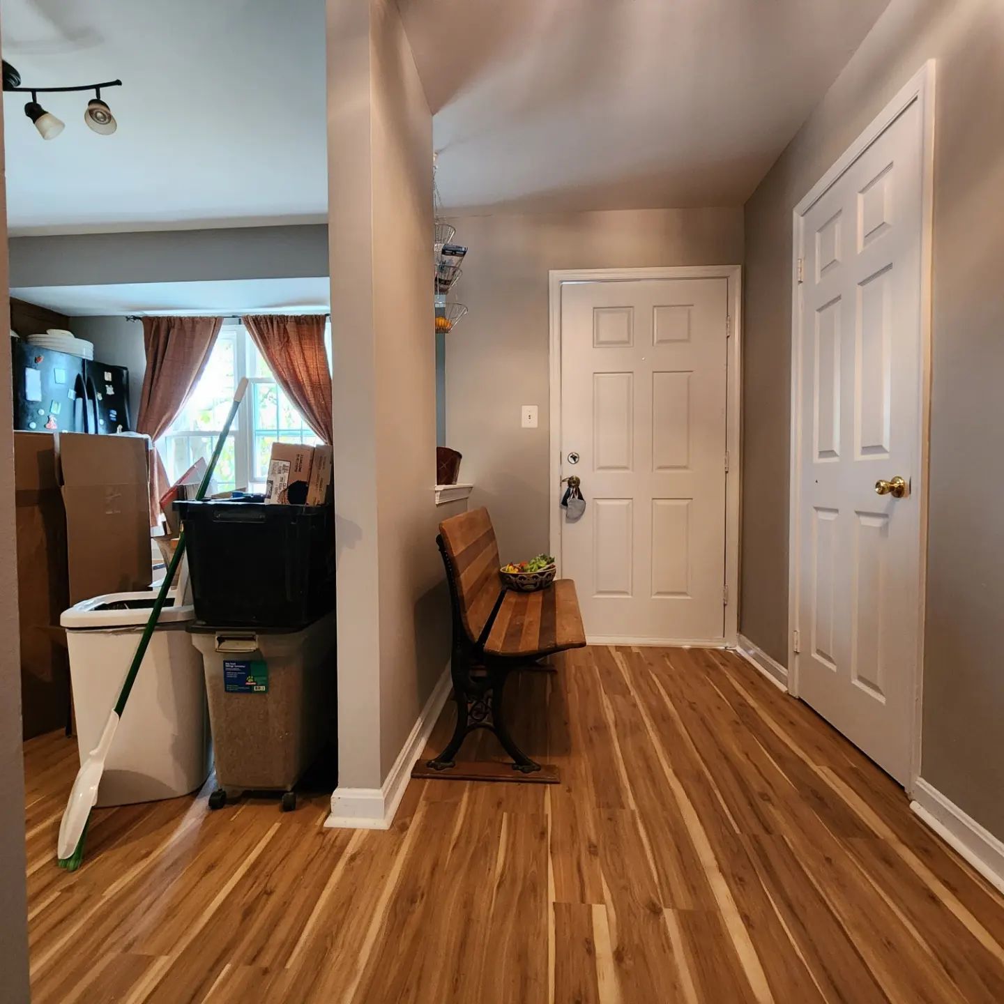 Hallway with wood floors, white doors, a bench, and a glimpse into a living room with curtains.