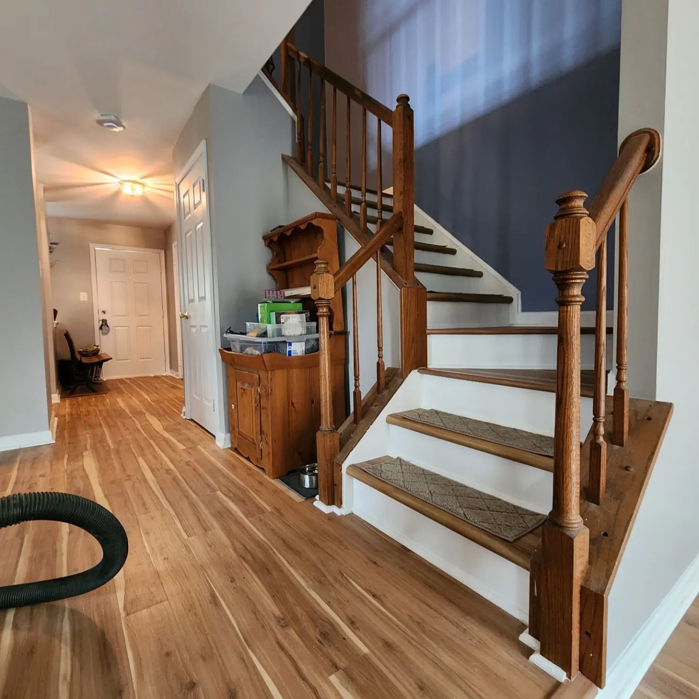 Hallway with wood floors and a white staircase with wooden banisters and a small cabinet underneath