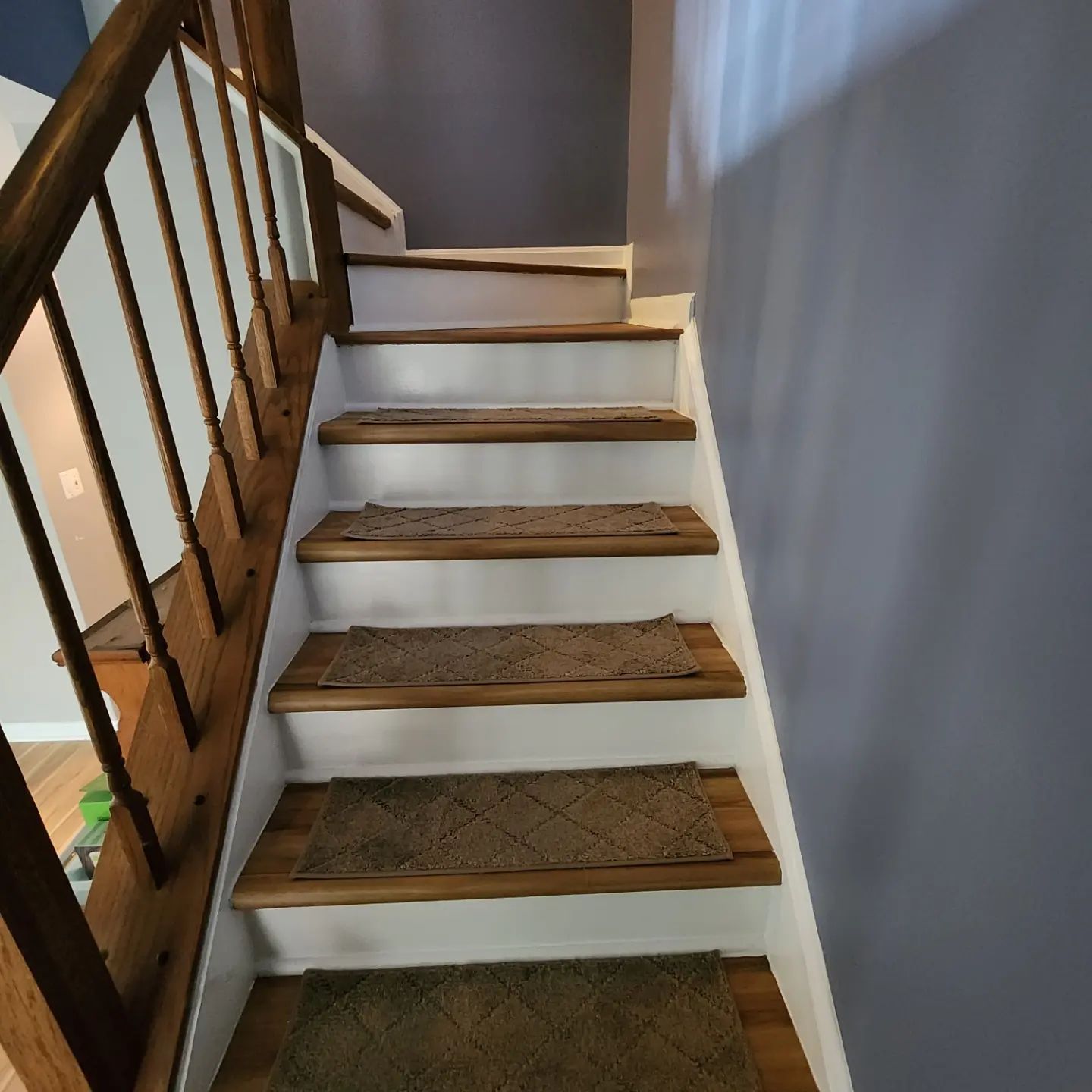 Indoor staircase with white risers, brown treads, and a dark wooden railing along a gray wall.